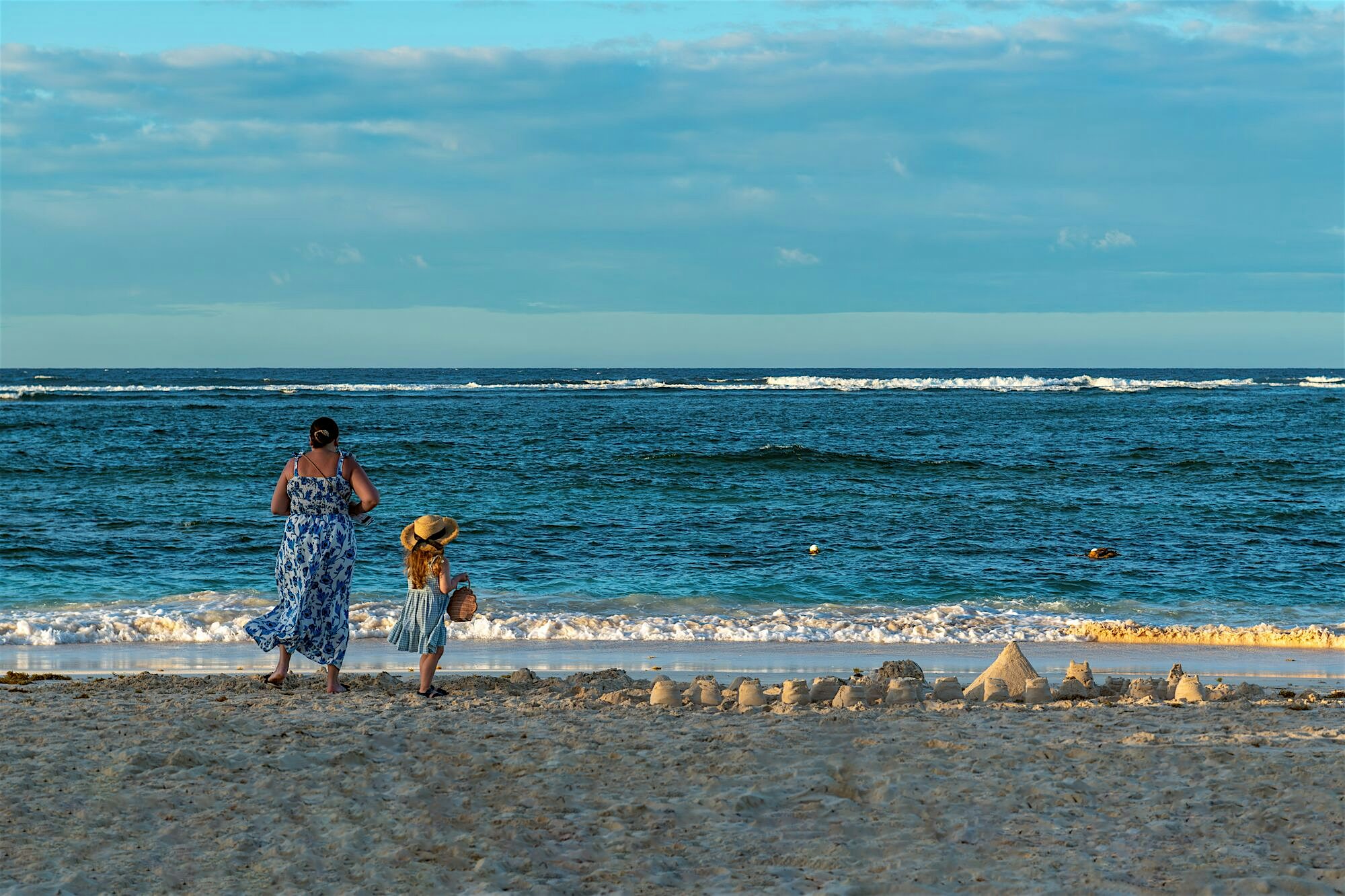 Mum and daughter looking out to the sea with sandcastles nearby
