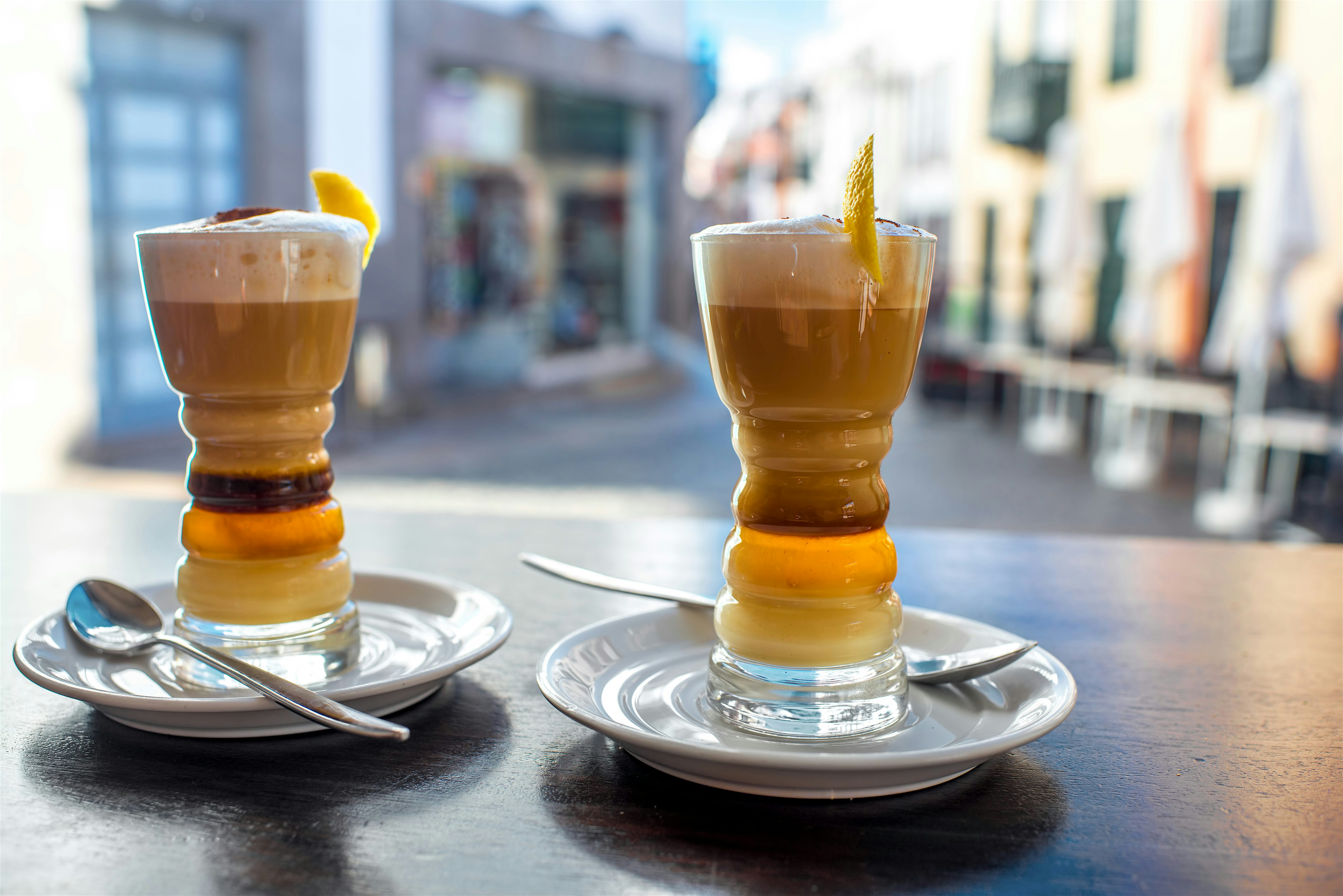 Two Barraquitos, a layered coffee liqueur drink garnished with a small piece of lemon peel.