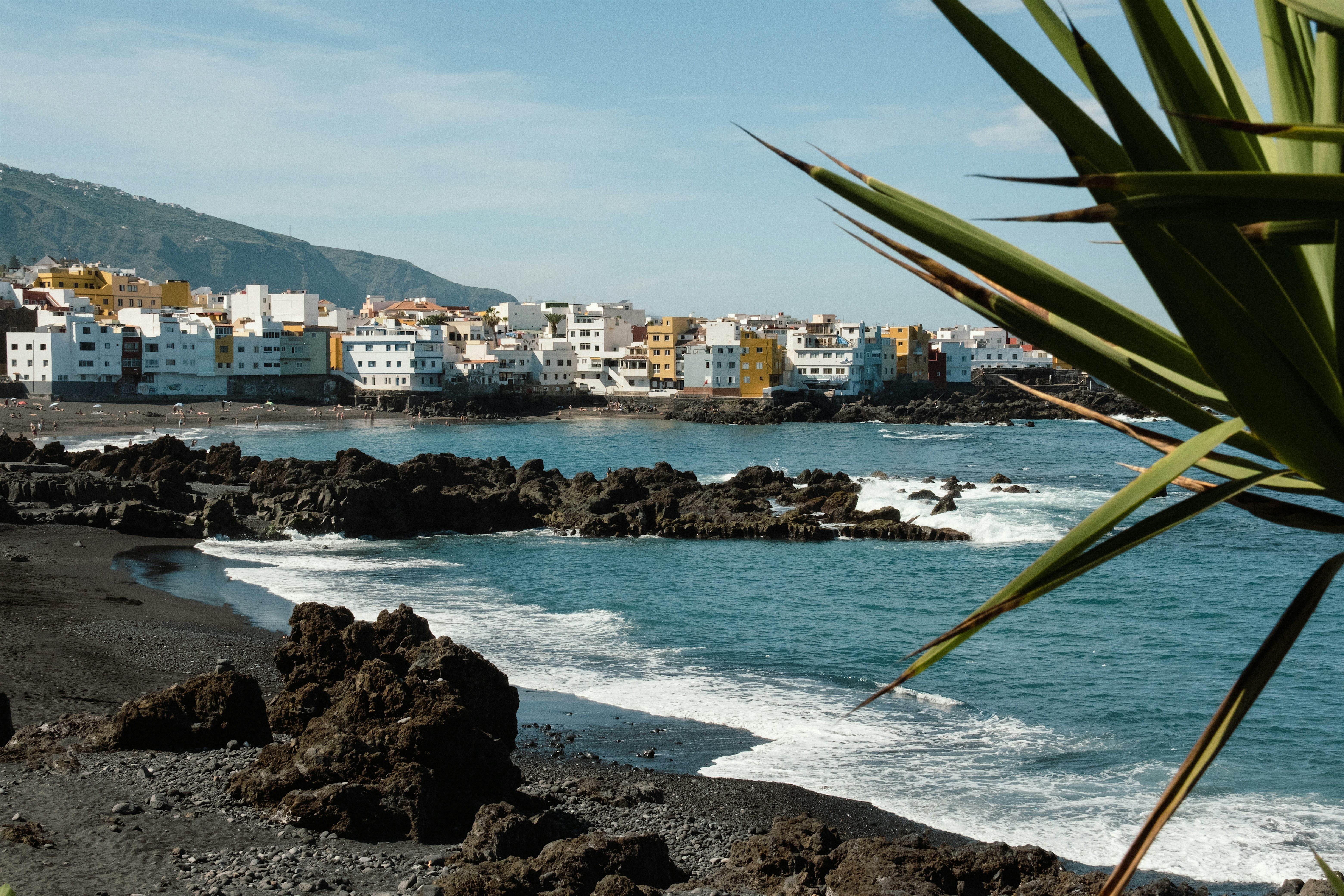 Playa Jardin beach black volcanic sand and rocks by the ocean. White and yellow buildings in the background.