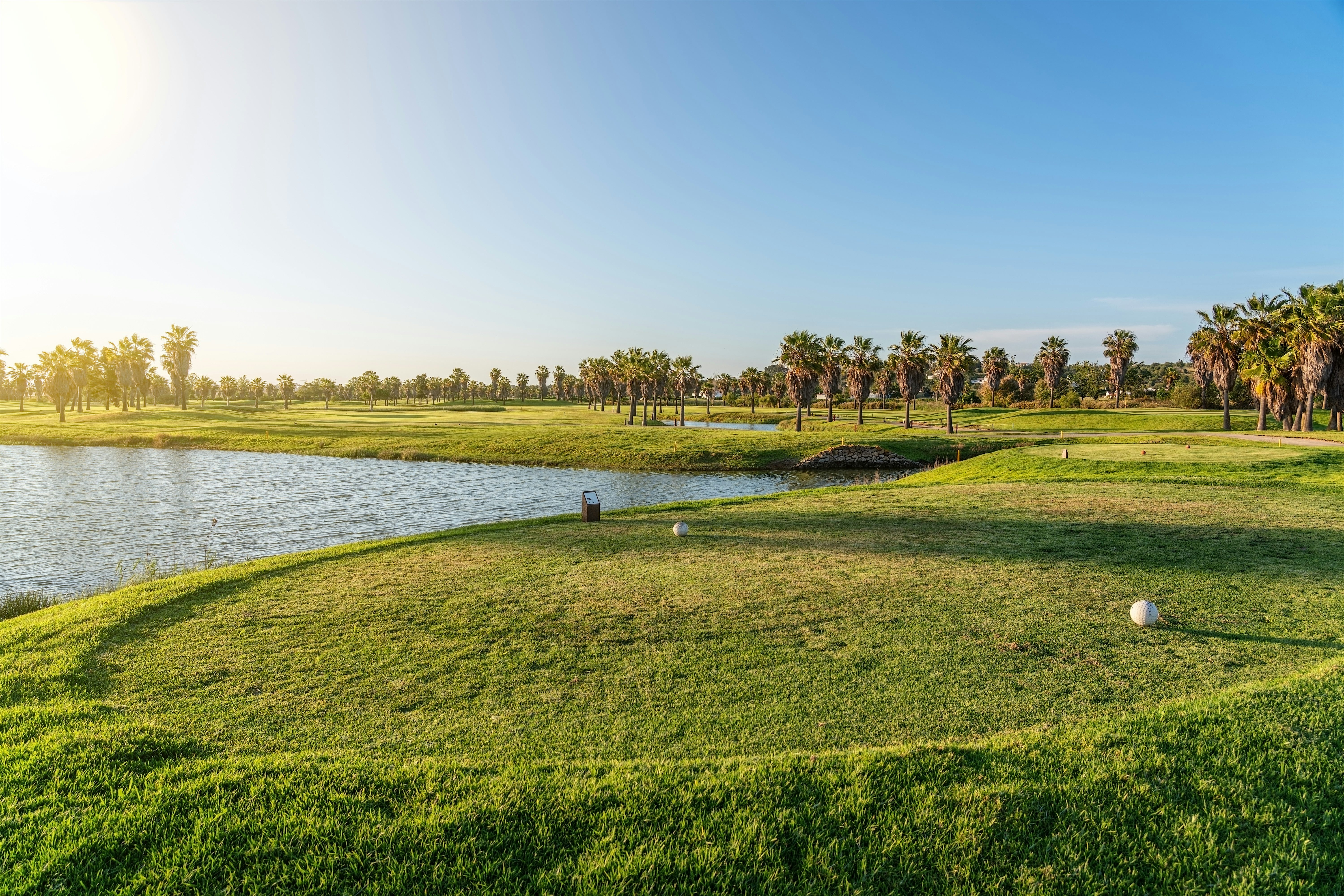 Open golf course with a wide green fairway beside calm water
