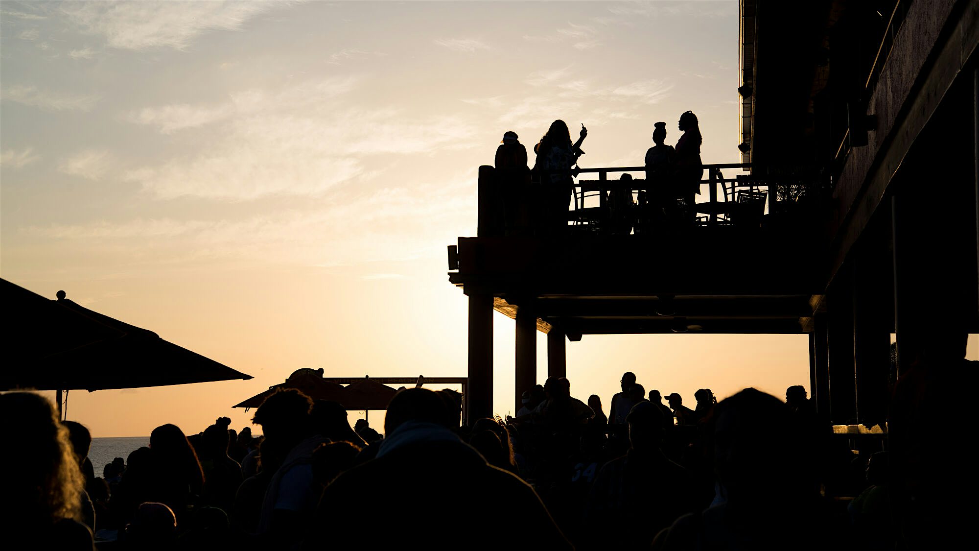Crowded waterfront venue with people watching the sunset over the Caribbean Sea