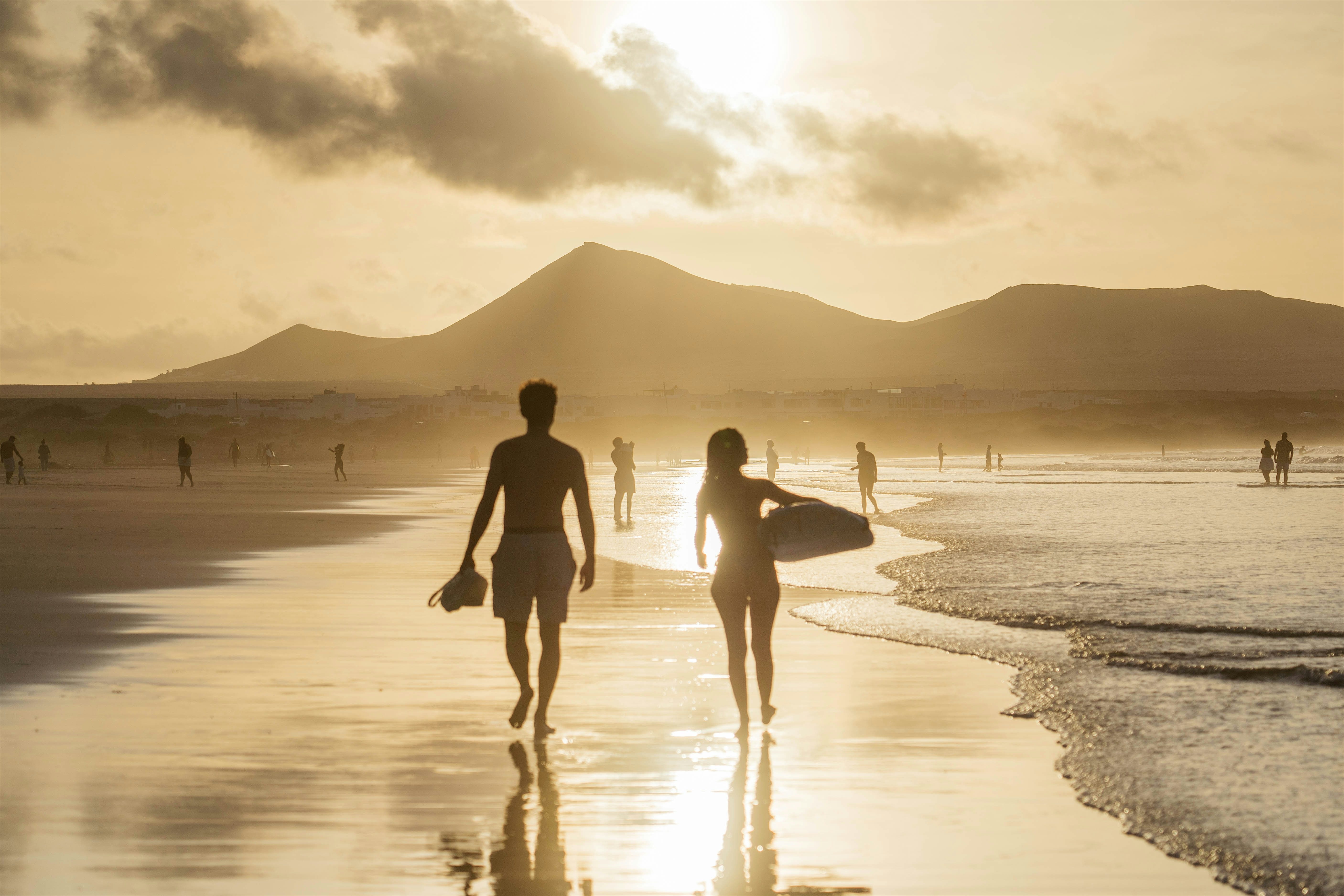 Surfers walking on the beach at sunset. Mountain range in the background.