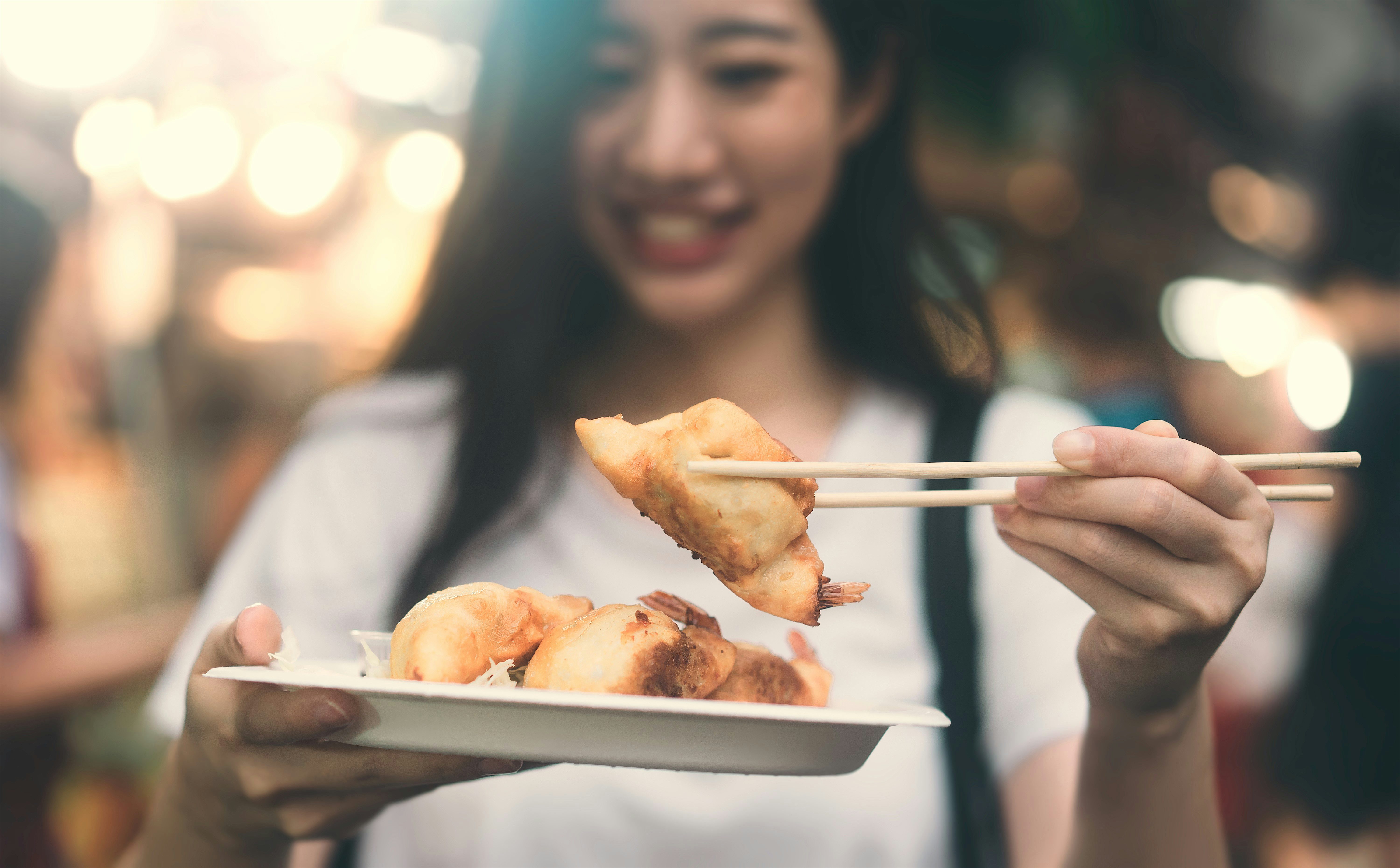 Woman holding a plate of dumplings (gyoza) and chopsticks. Blurred background of a night market