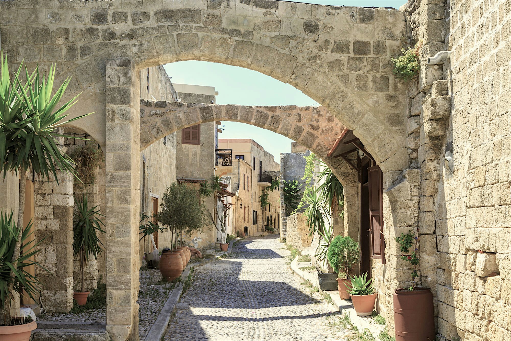 Medieval Old Town of Rhodes narrow street, cobbled pathway, and Gothic stone architecture archways with plants in pots lining the sides