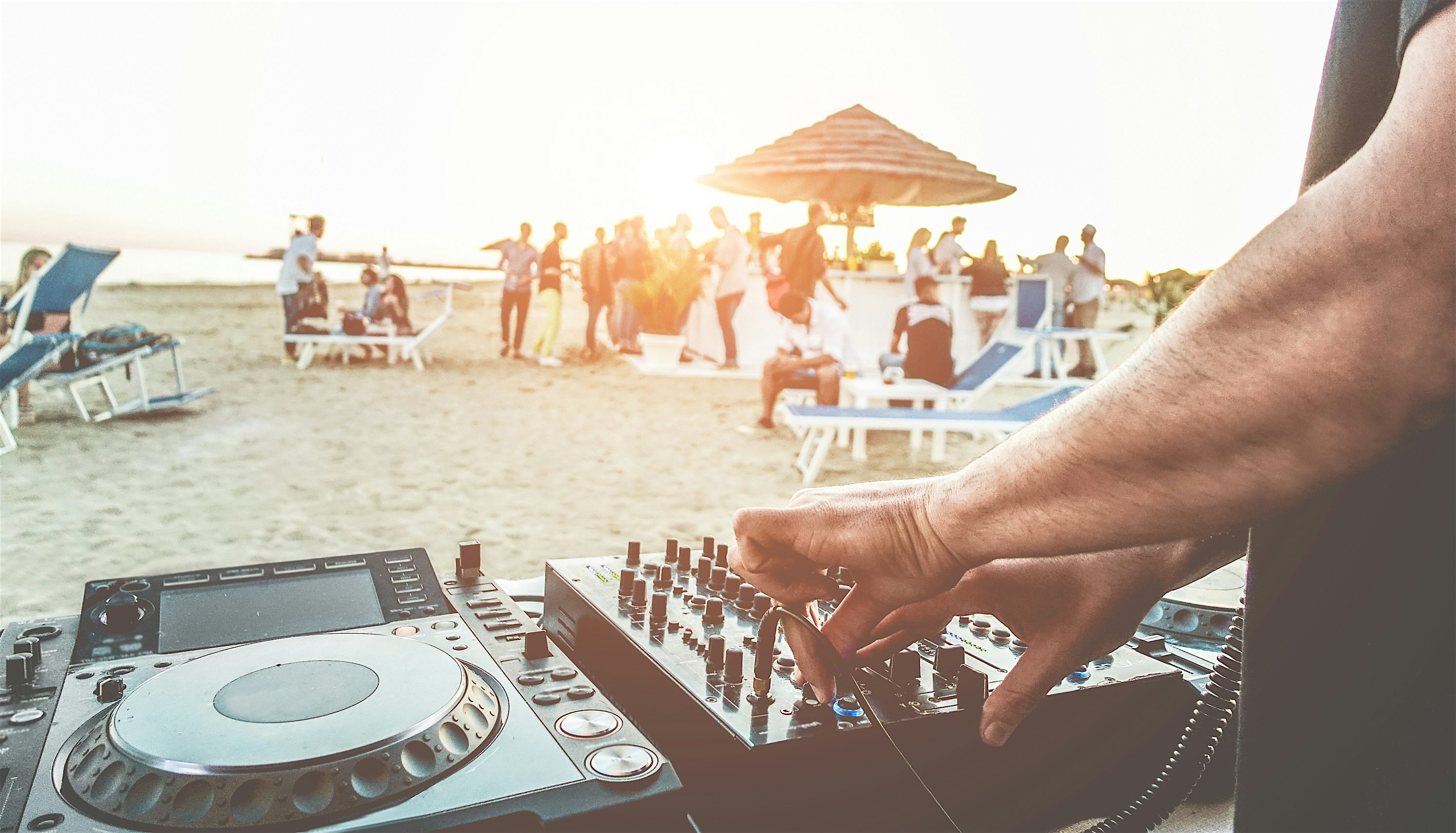 DJ playing to people on the beach with sunlounges and a tropical bar at sunset