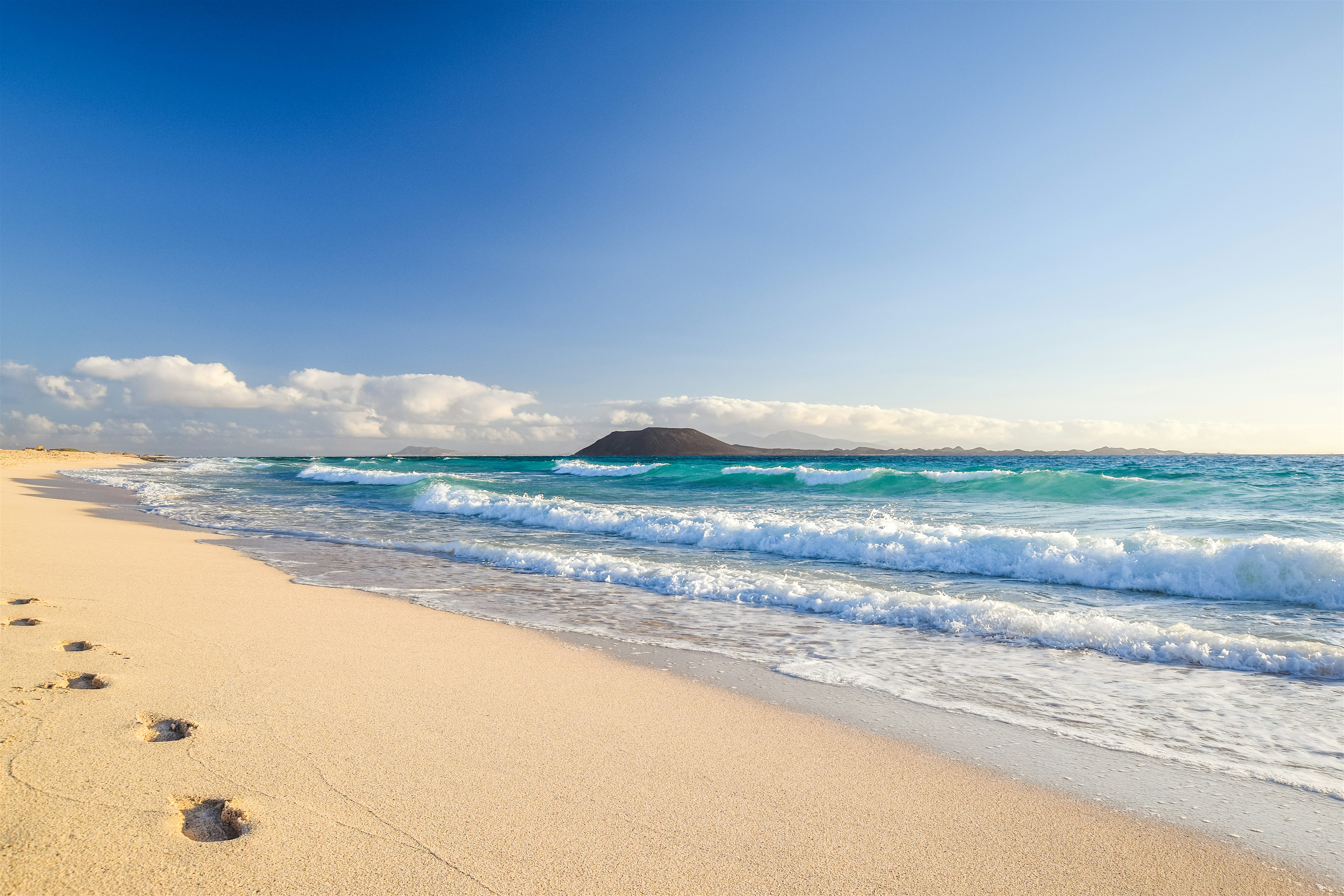 Empty sandy beach, rolling waves. In the distance, the volcanic Isla de Lobos.