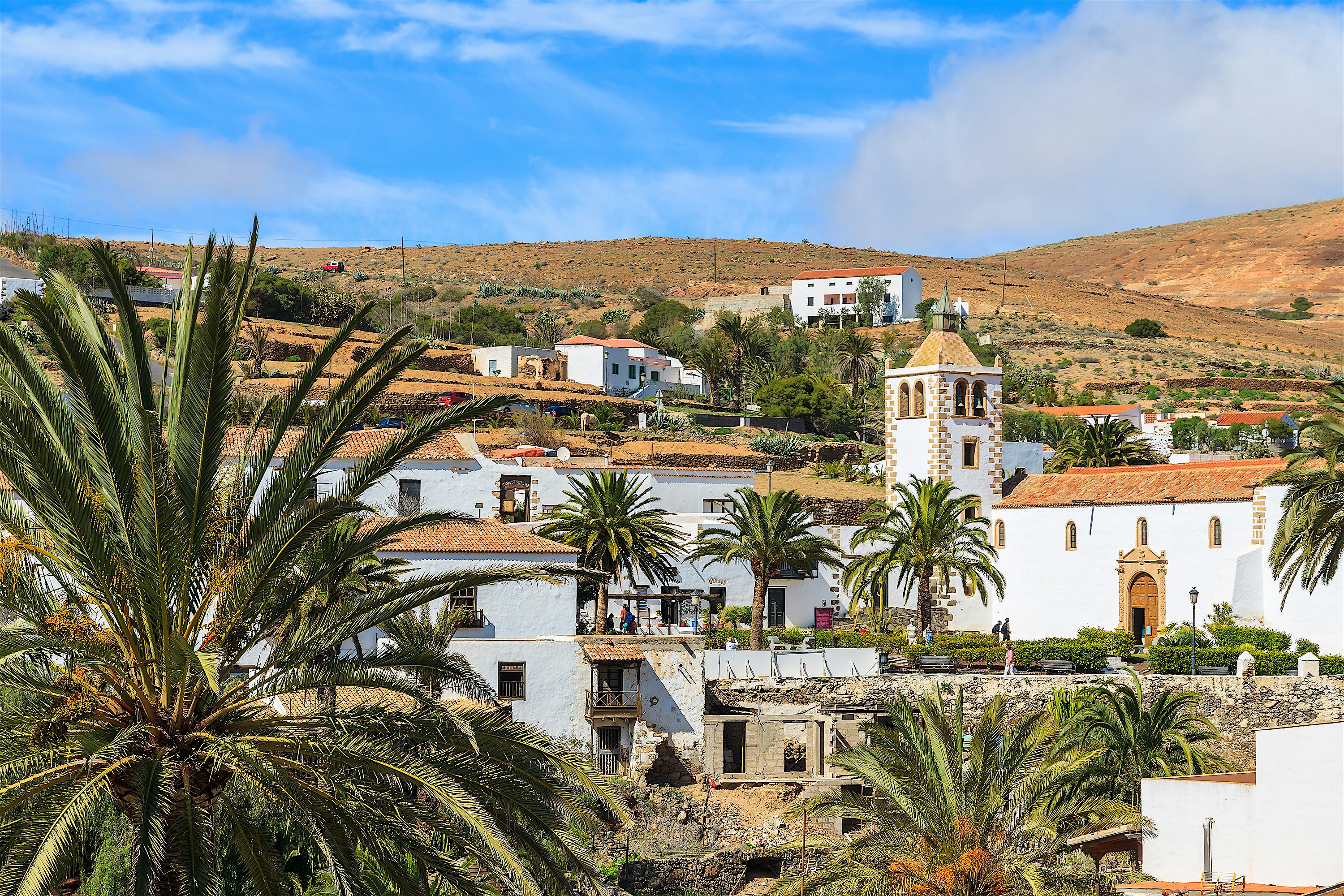 Church of Santa Maria de Betancuria white building with a tower. Palm trees inbetween traditional buildings.