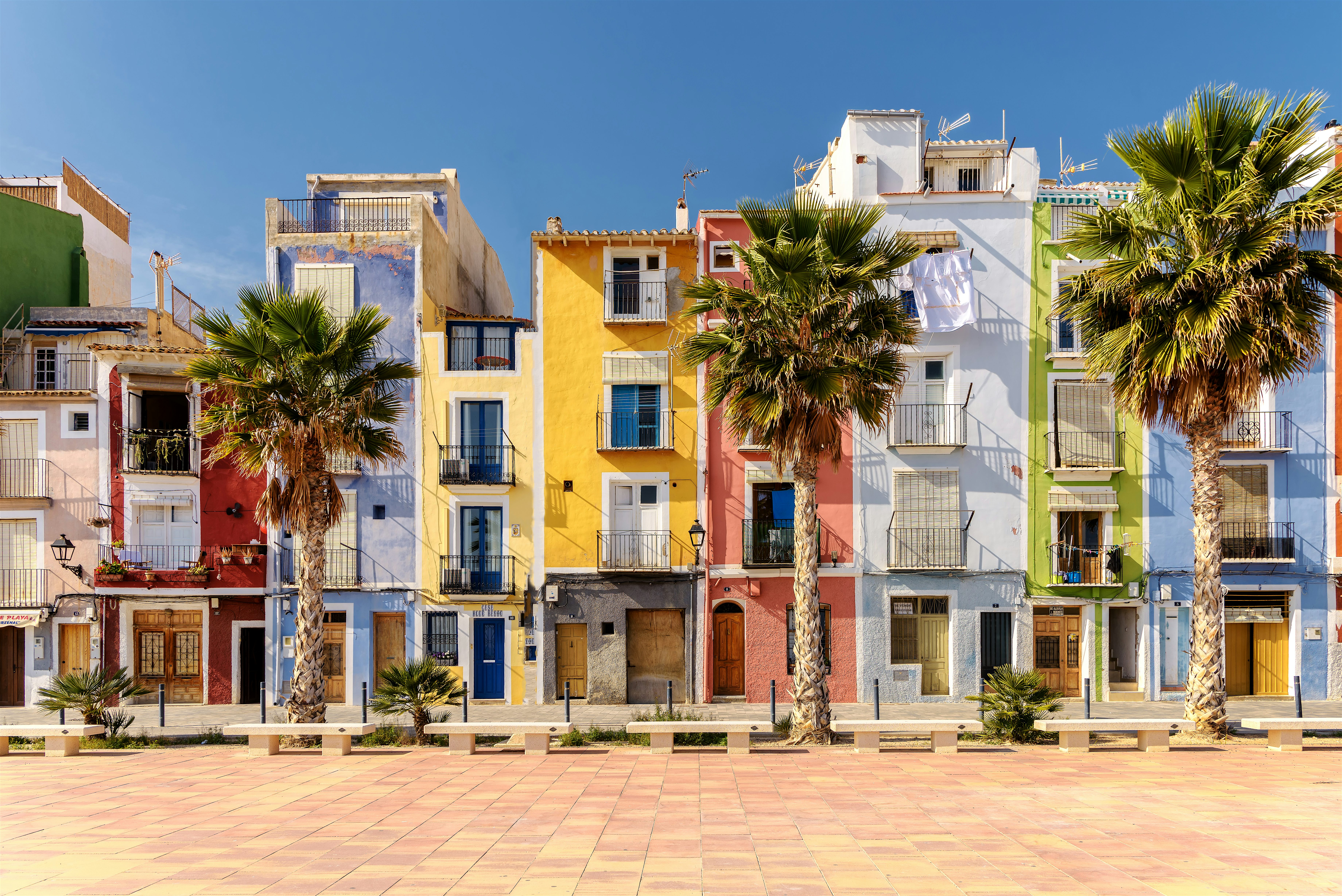 Colourful apartment buildings lined up along a promenade, with palm trees in front and balconies facing an open plaza.