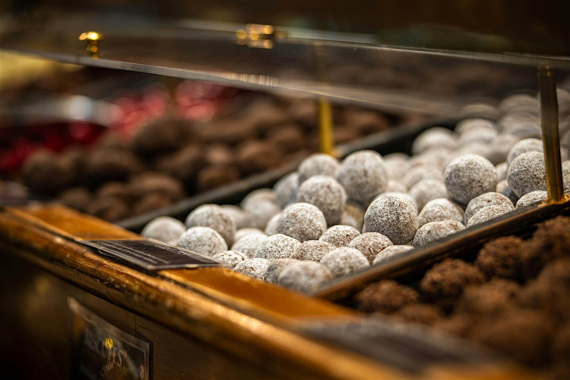 Close-up of powdered chocolate truffles displayed neatly in a glass counter, arranged alongside darker cocoa-coated varieties.