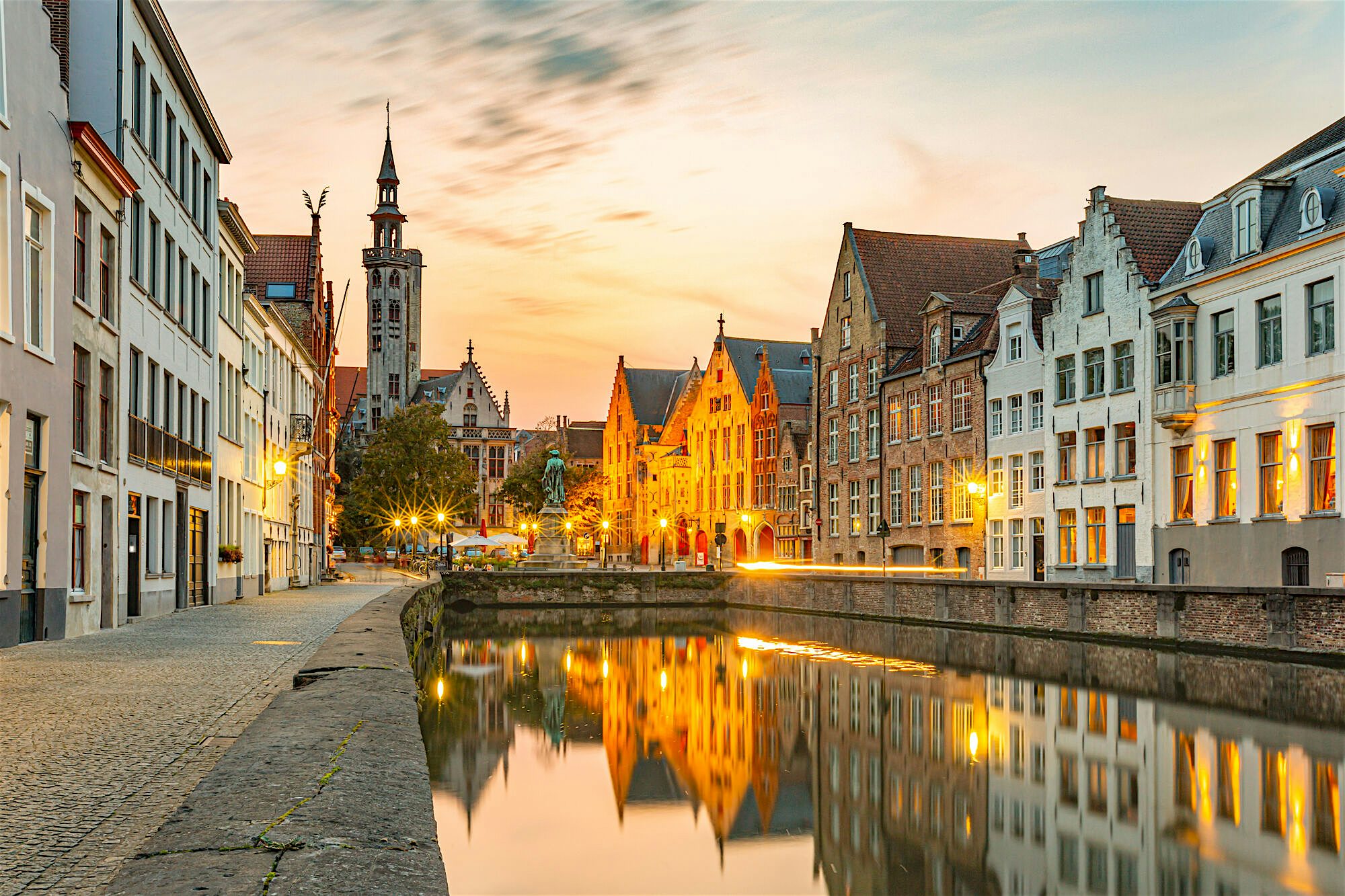 Quiet canal lined with historic buildings reflecting perfectly in still water at sunset, old town architecture glowing softly.