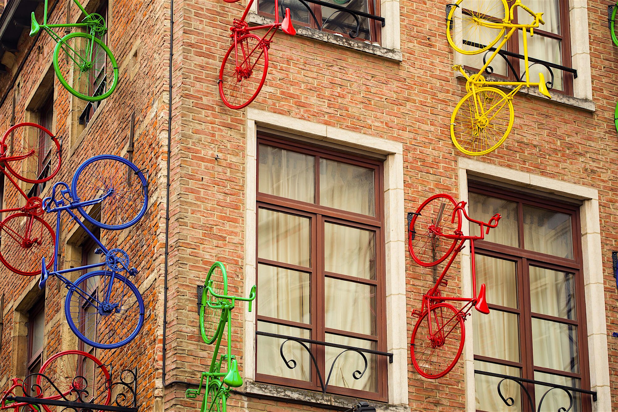 Brick building façade decorated with brightly coloured bicycles mounted to the walls, creating a playful street art installation.