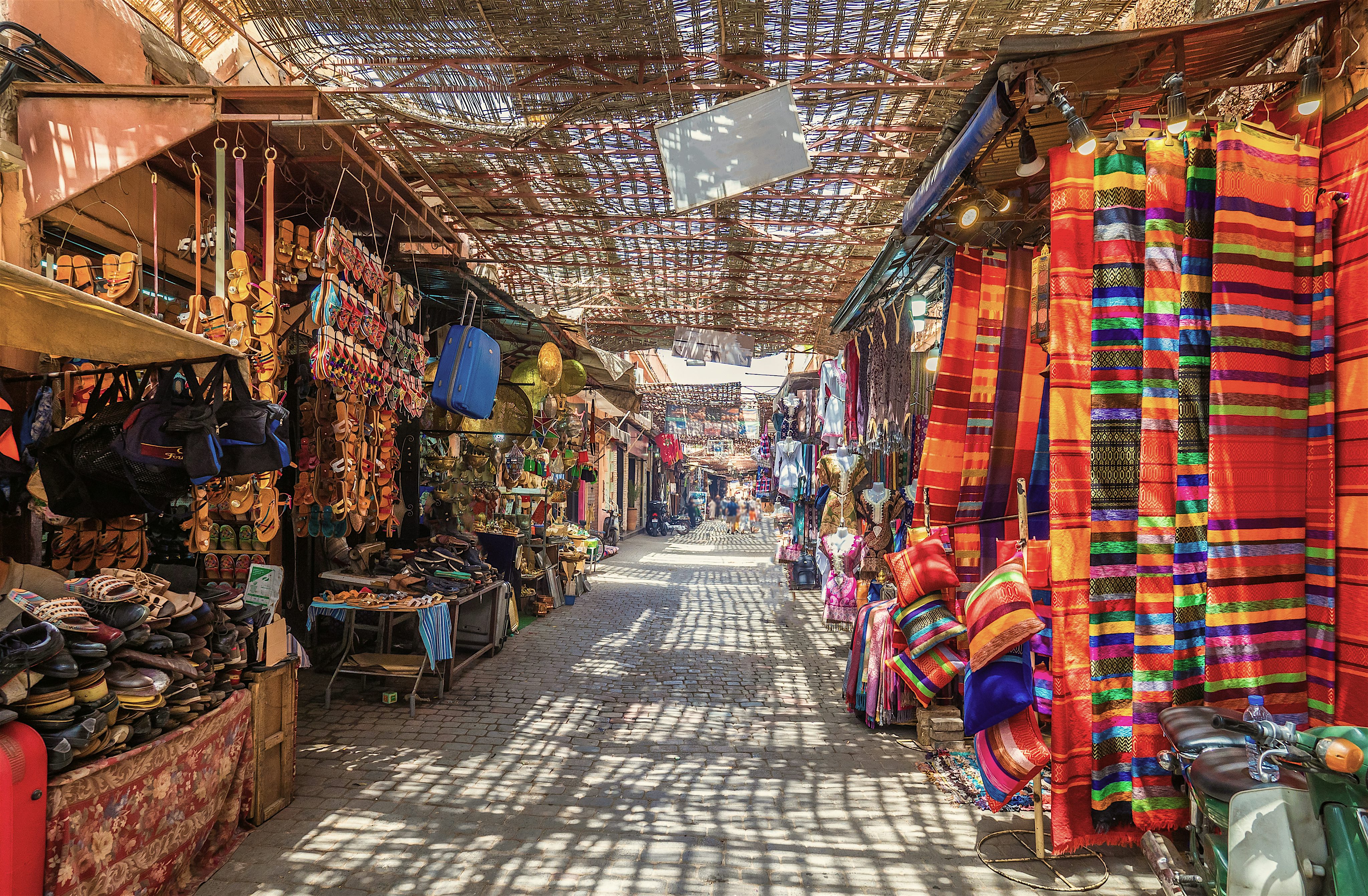 Pathway through a market with  leather shoes, bags and colourful fabrics
