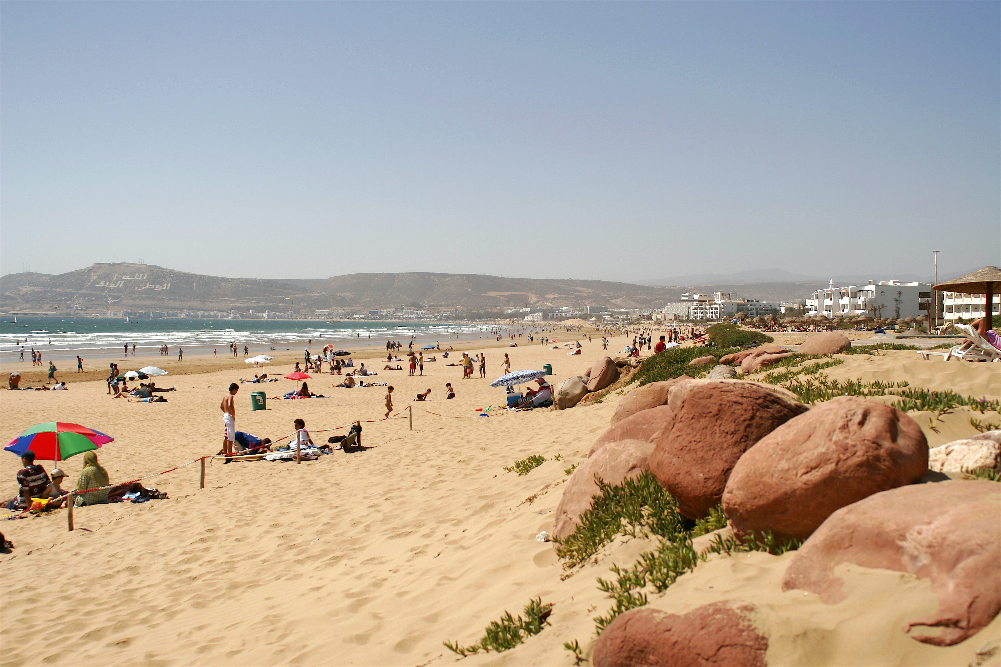 Sandy golden beach with large rocks in the forefront and hills at the end of the bay