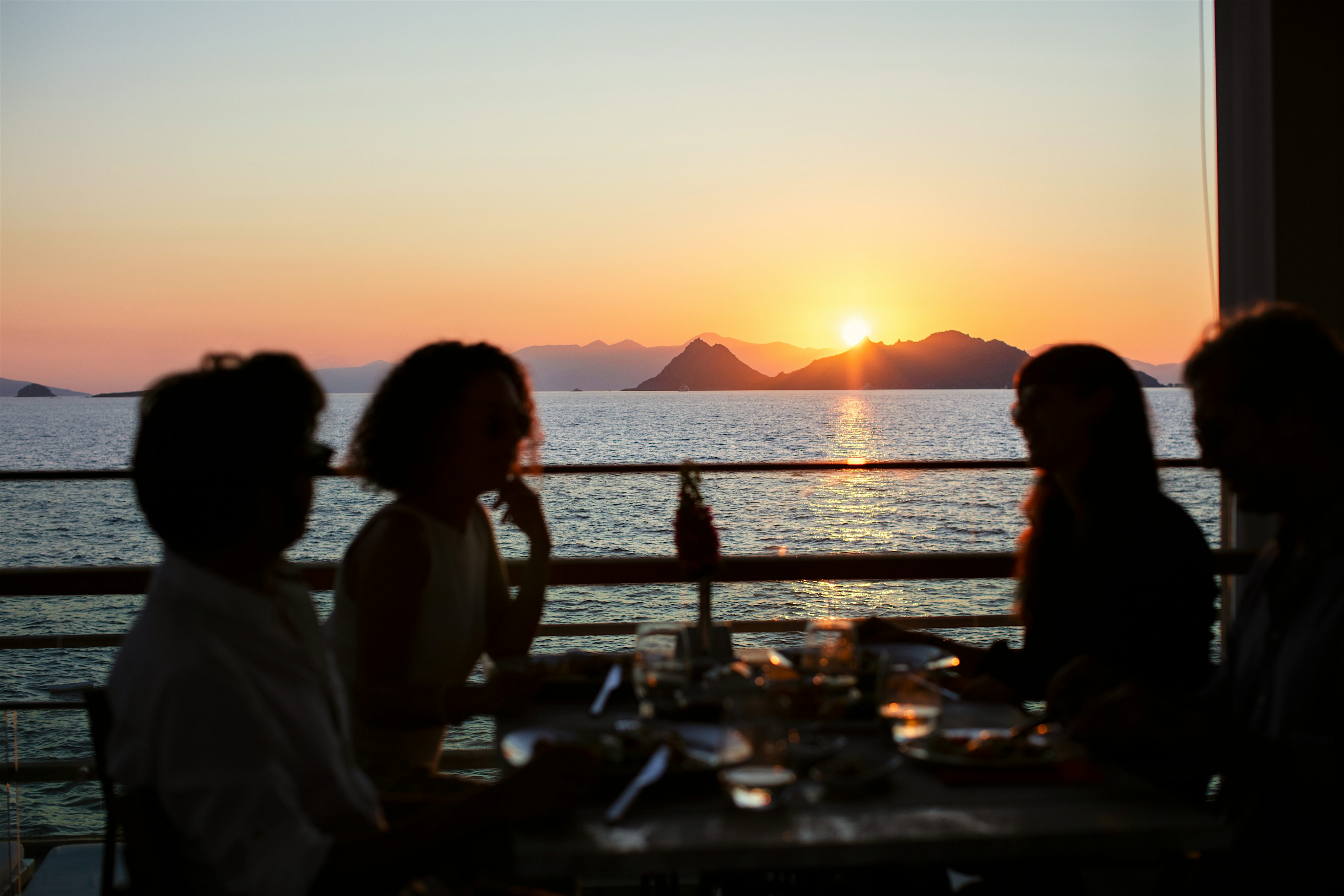 Silhouette view of people at a table overlooking the ocean watching the sunset