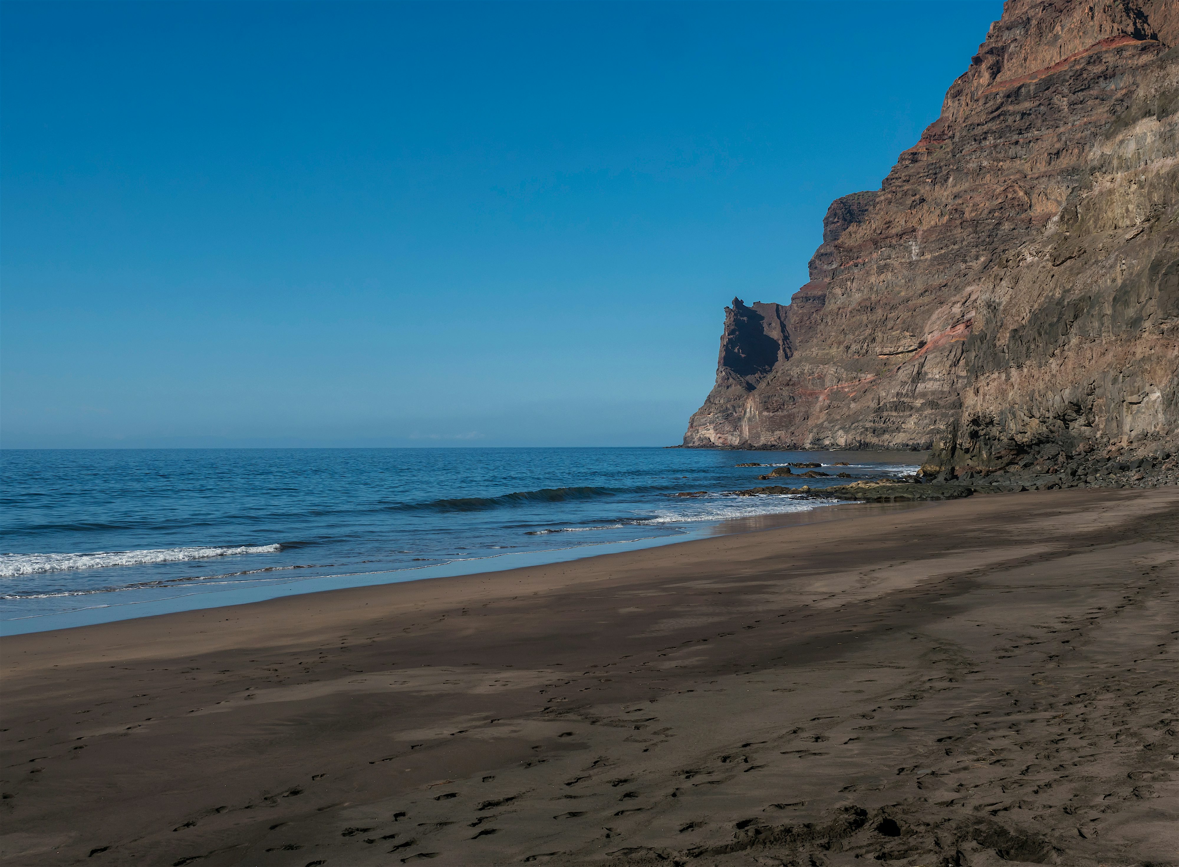 Empty remote beach with dark sand and volcanic cliff