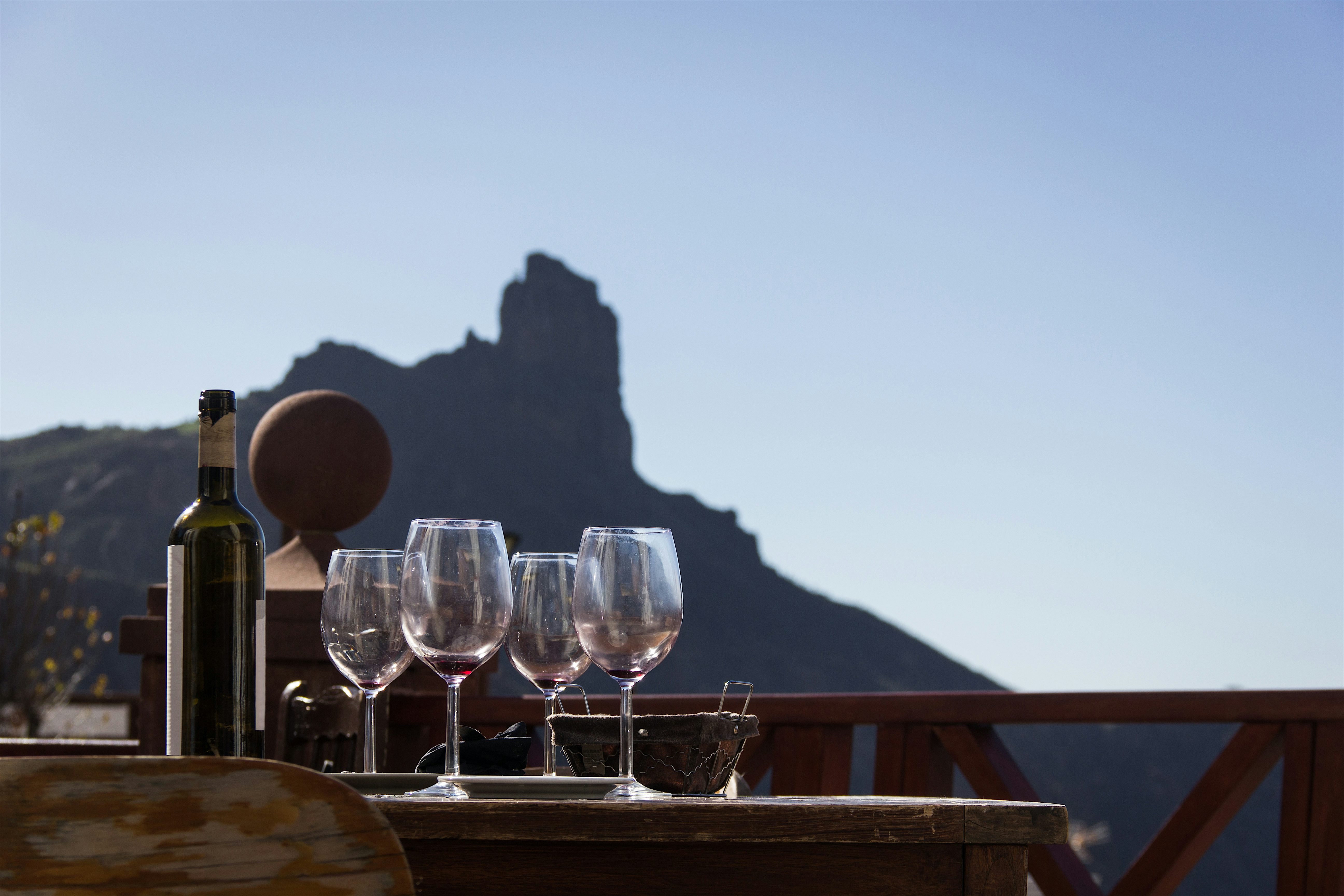 Bottle of wine and 4 empty wine glasses after a tasting. Volcanic rock formation in the background.