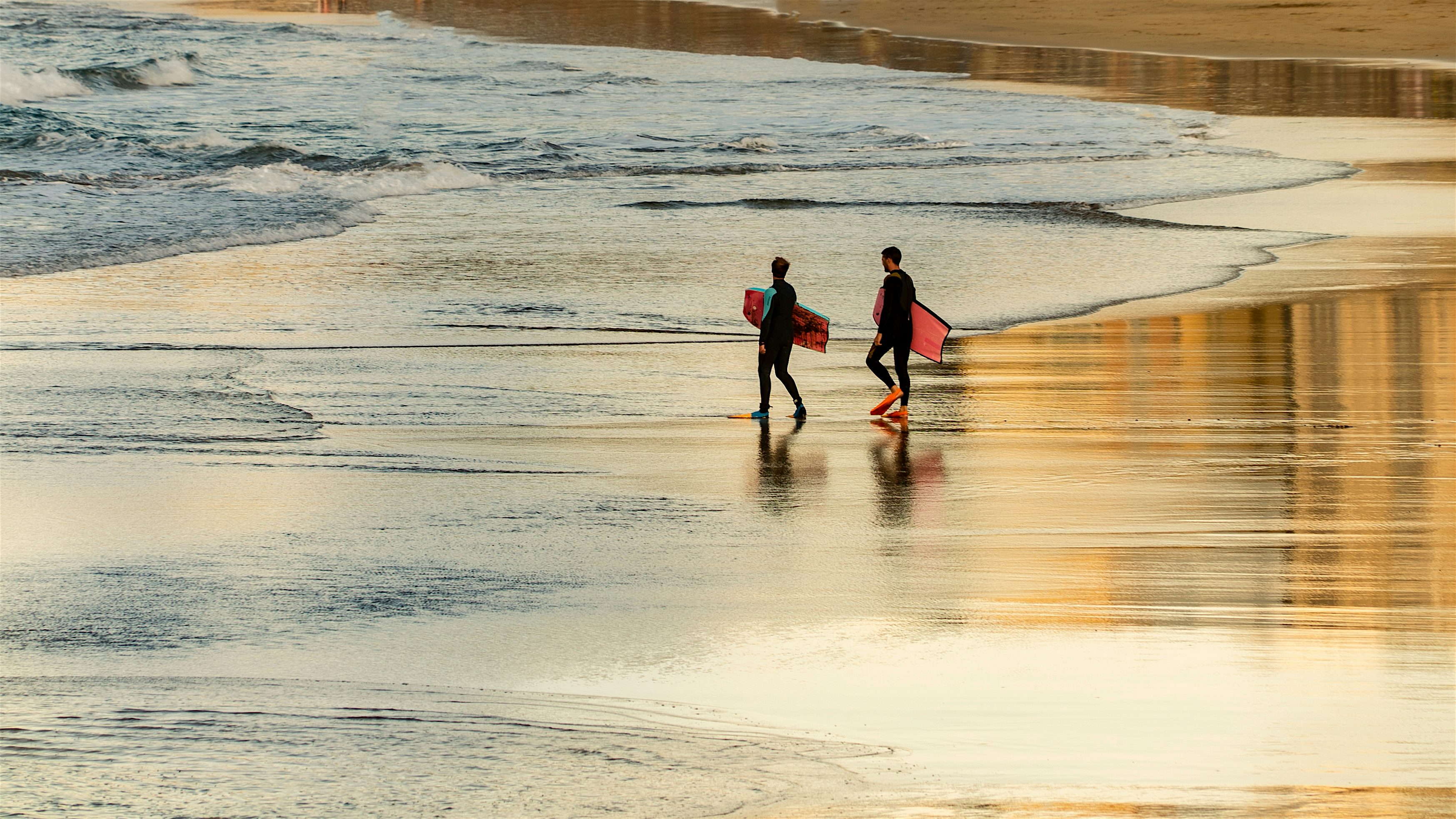 Two surfers walking across the wet sand into the water