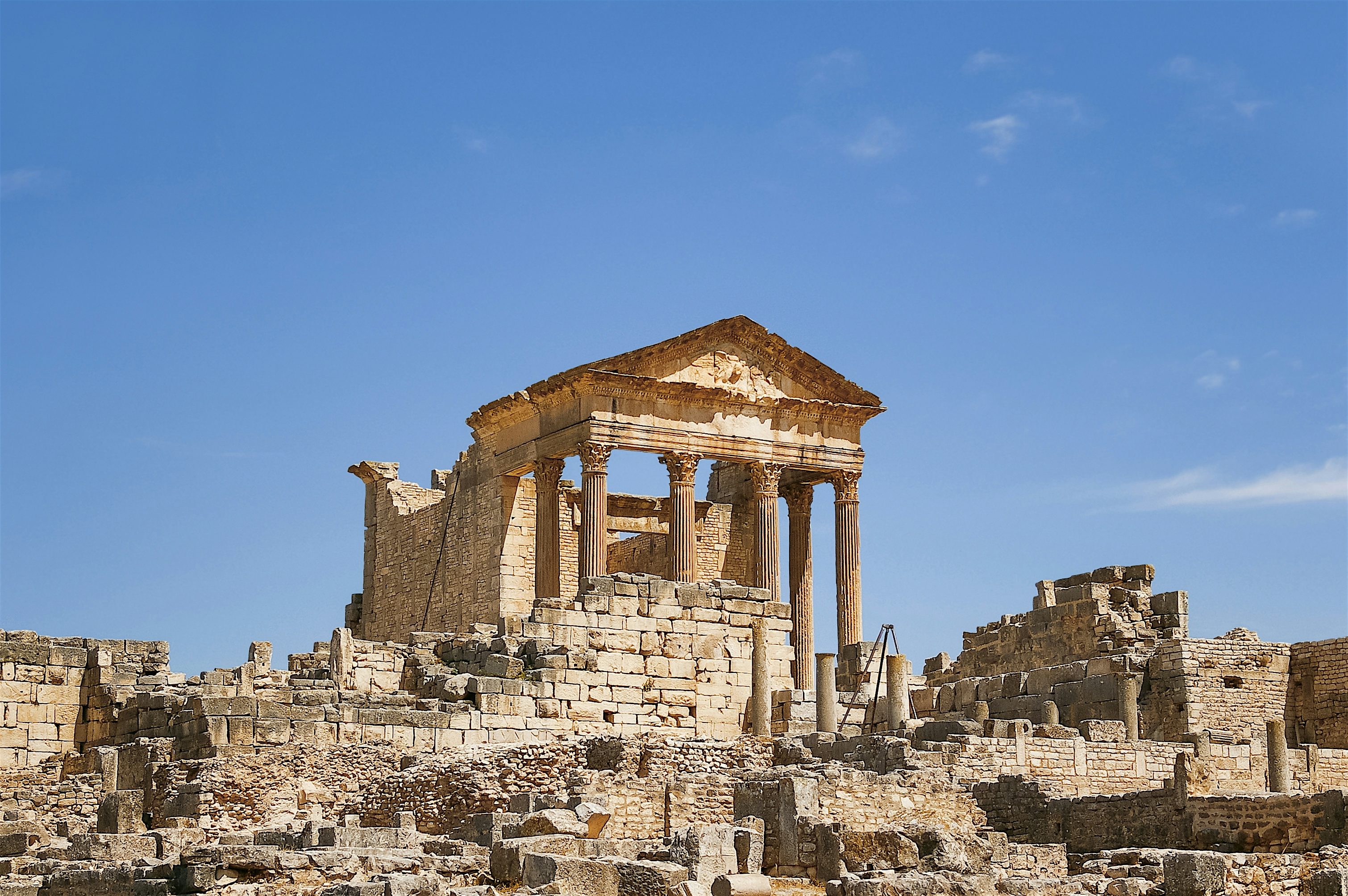 Ancient Roman temple ruins with tall columns standing on a rocky hillside under a clear blue sky