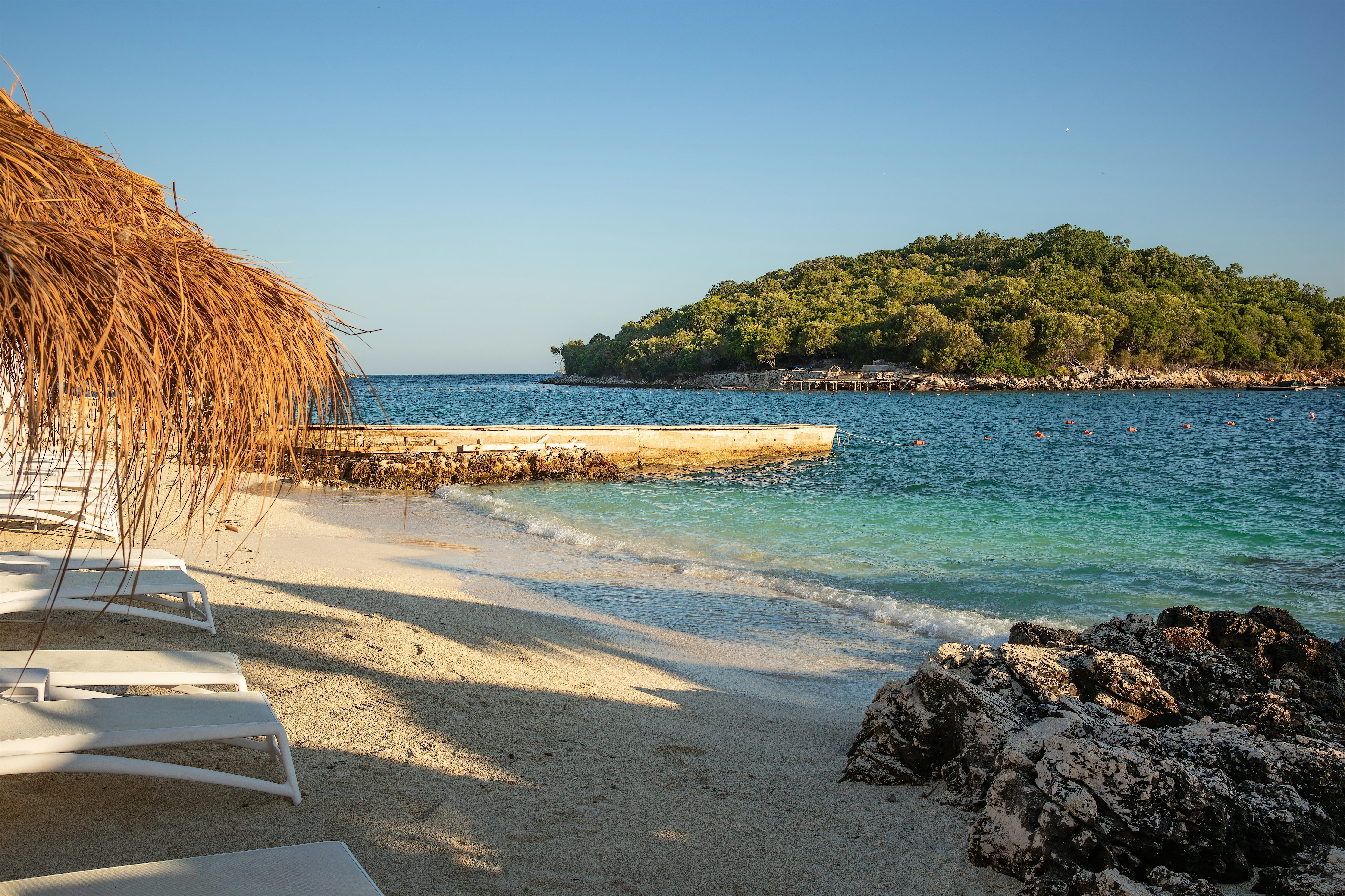 Ksamil Island Sunny morning on a sandy beach with straw umbrellas and sunlounges by a turquoise sea and little island opposite