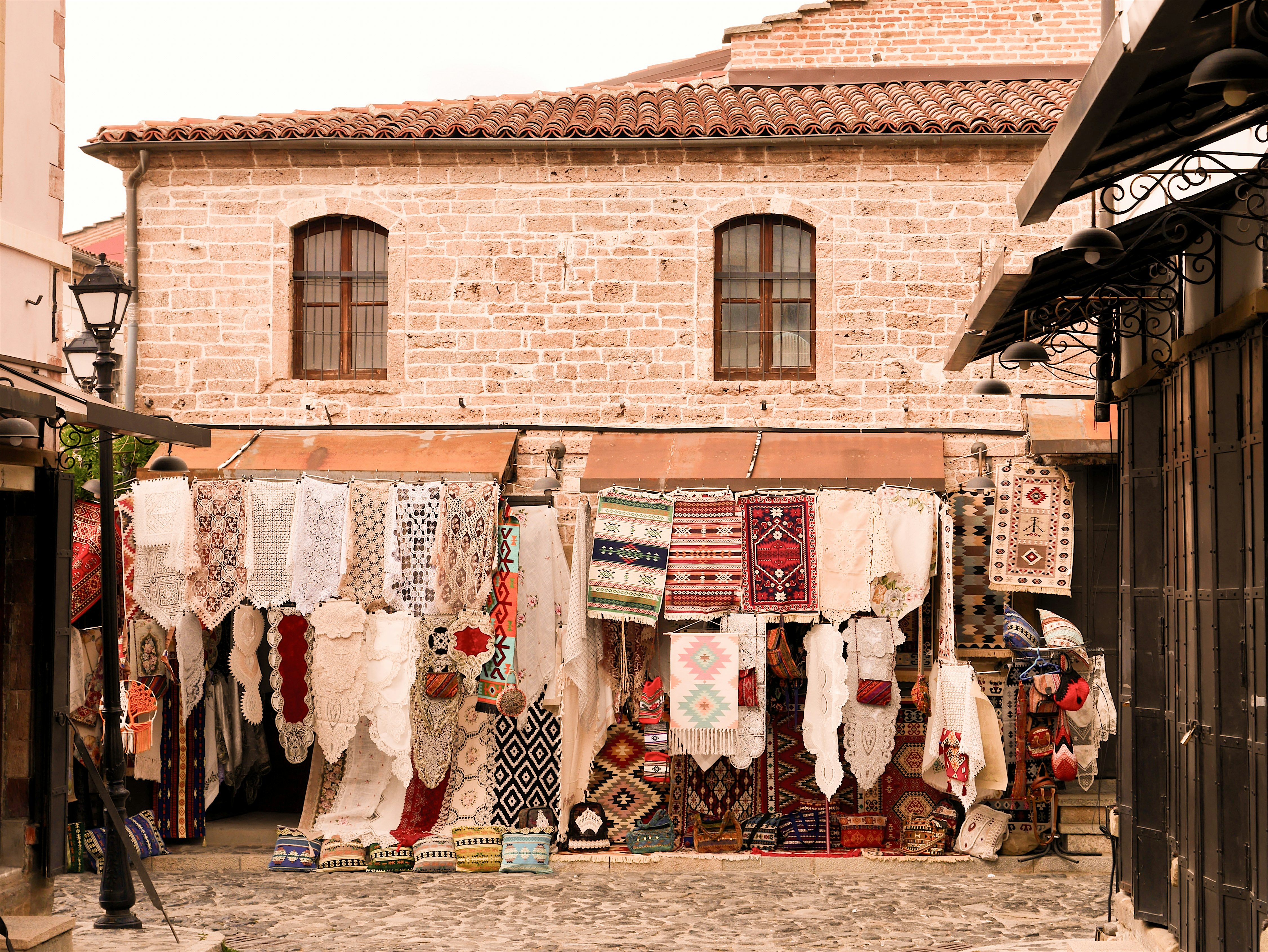 Old Bazaar of Korçë traditional stone buildings, cobblestone streets, and characteristic windows with traditional rugs, carpets, and lace textiles on display outside