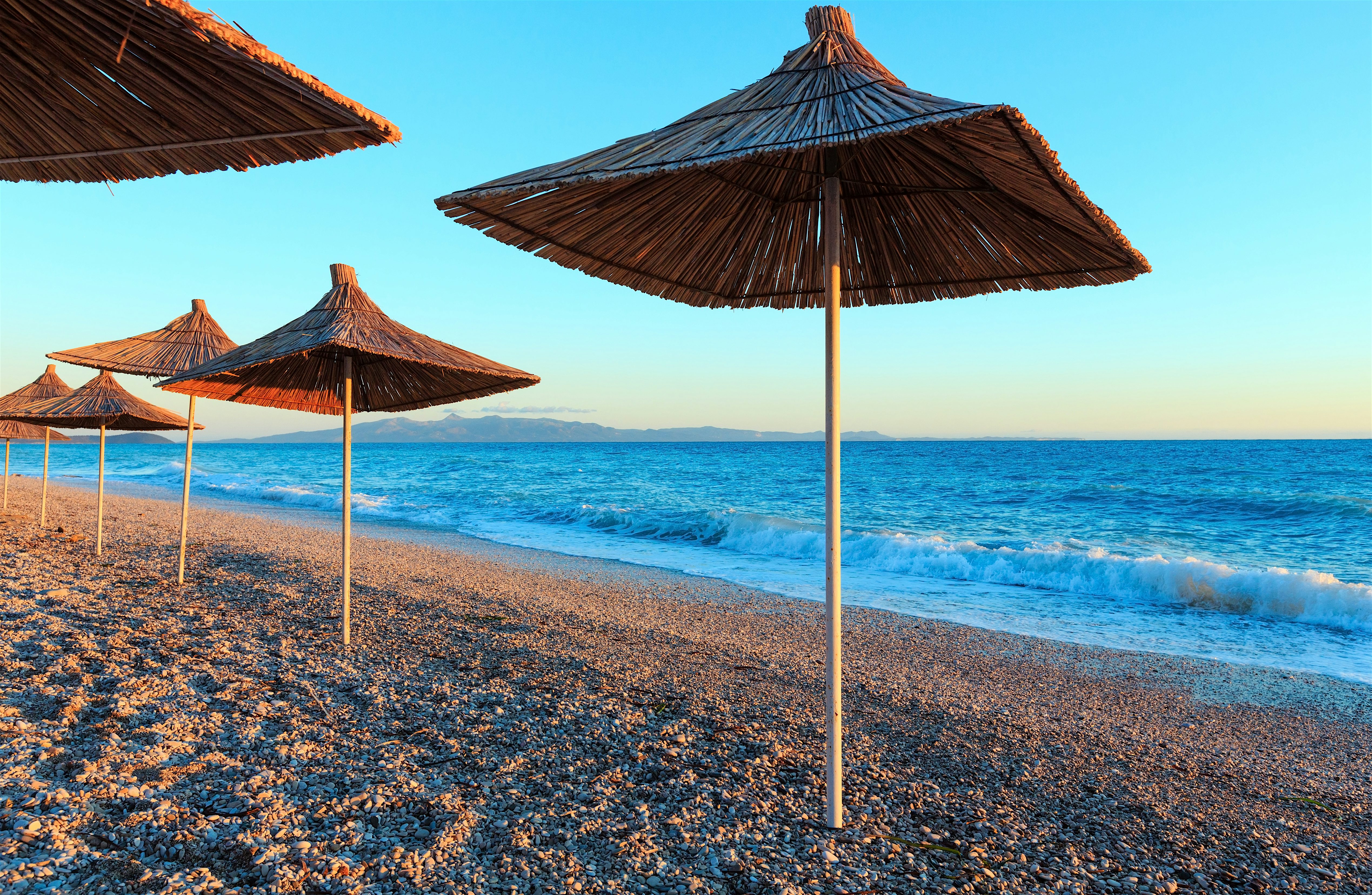 Borsh Pebbly beach with straw parasols. Blue sea with mountains in the distant background.