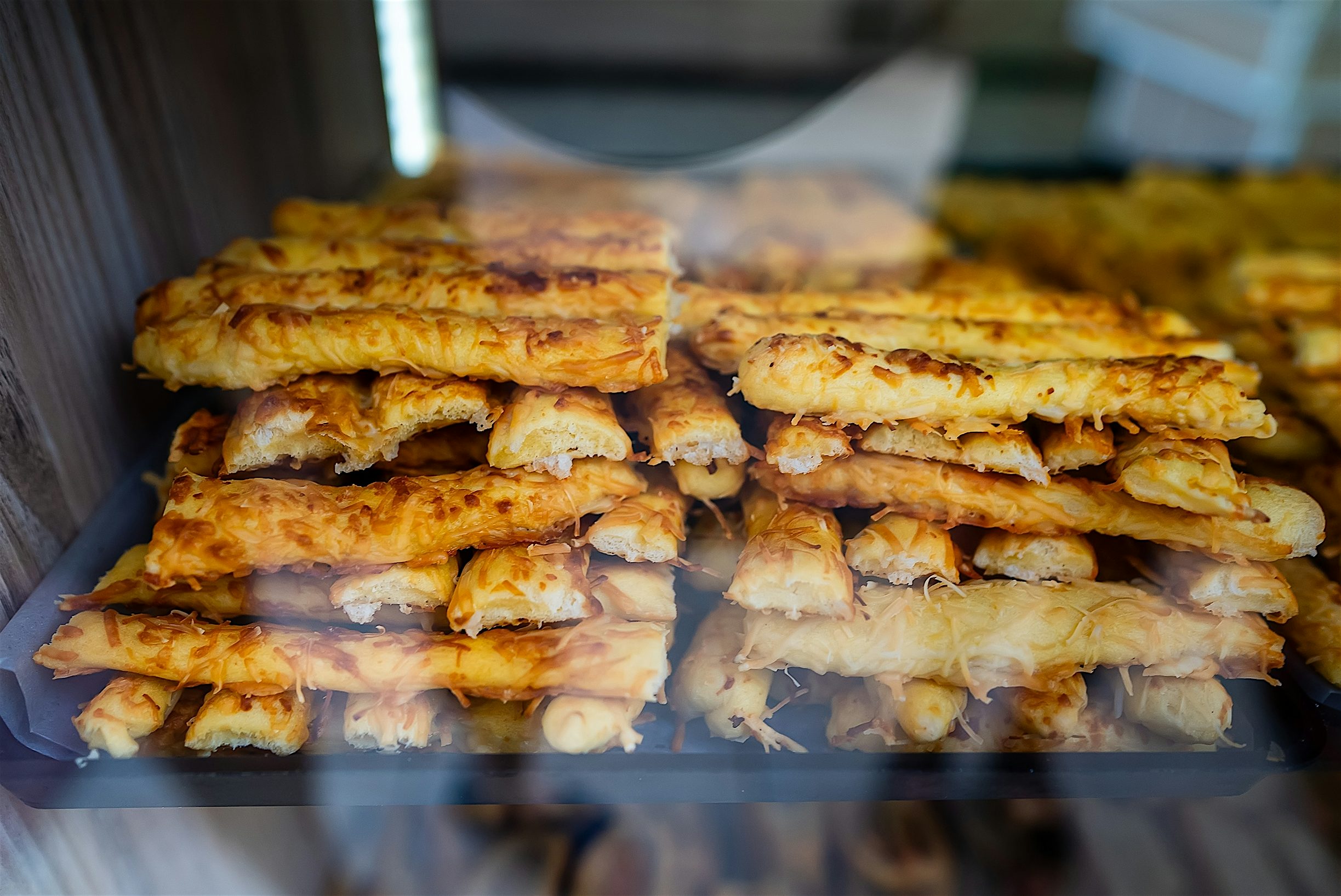 Byrek cheese topped filo pastry sticks stacked in rows displayed in a bakery window.