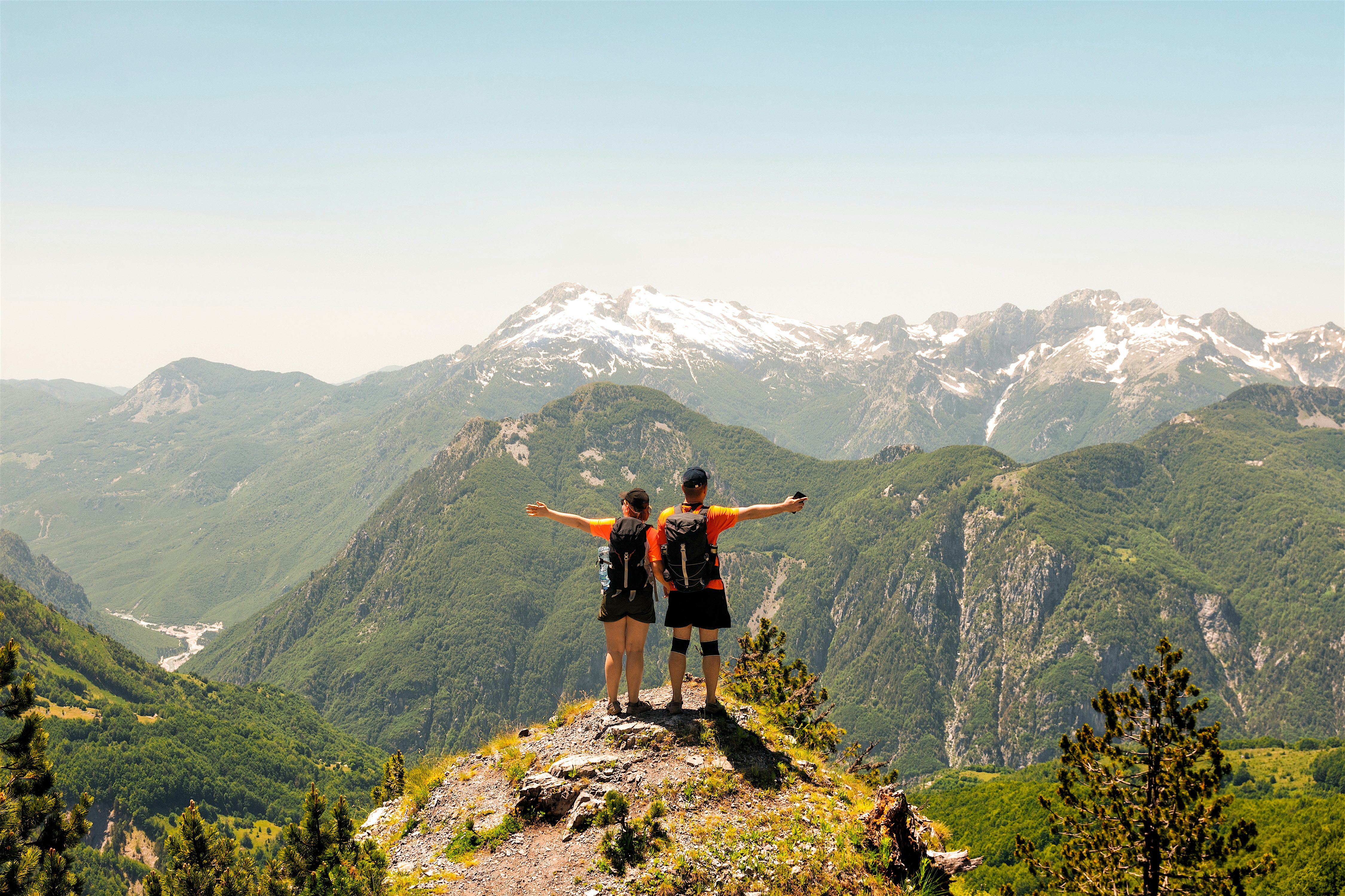 2 hikers looking out at the Valbona Valley with snow capped mountains