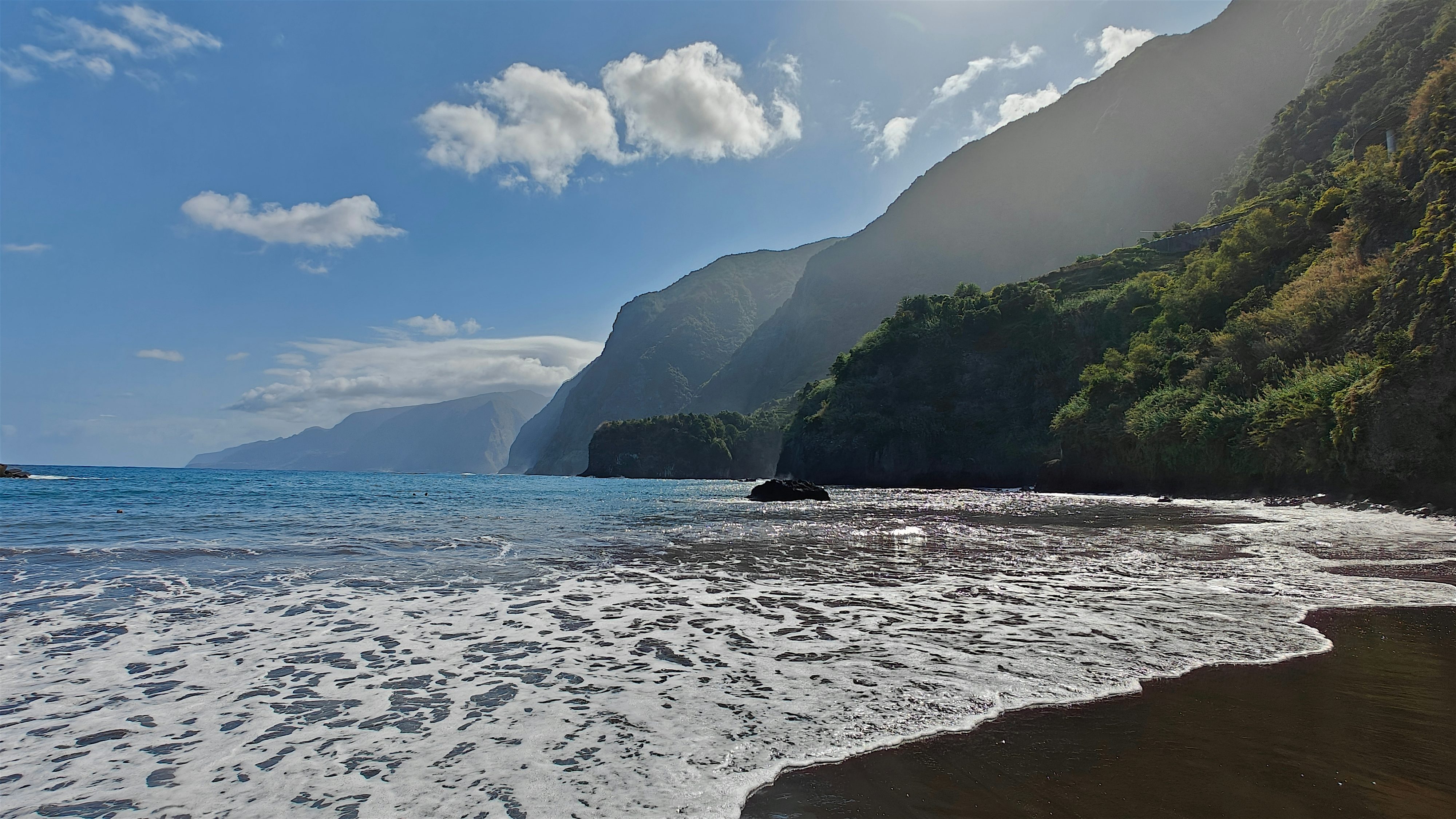 Praia do Porto do Seixal, a black sand beach by lush green cliffs that drop into the ocean
