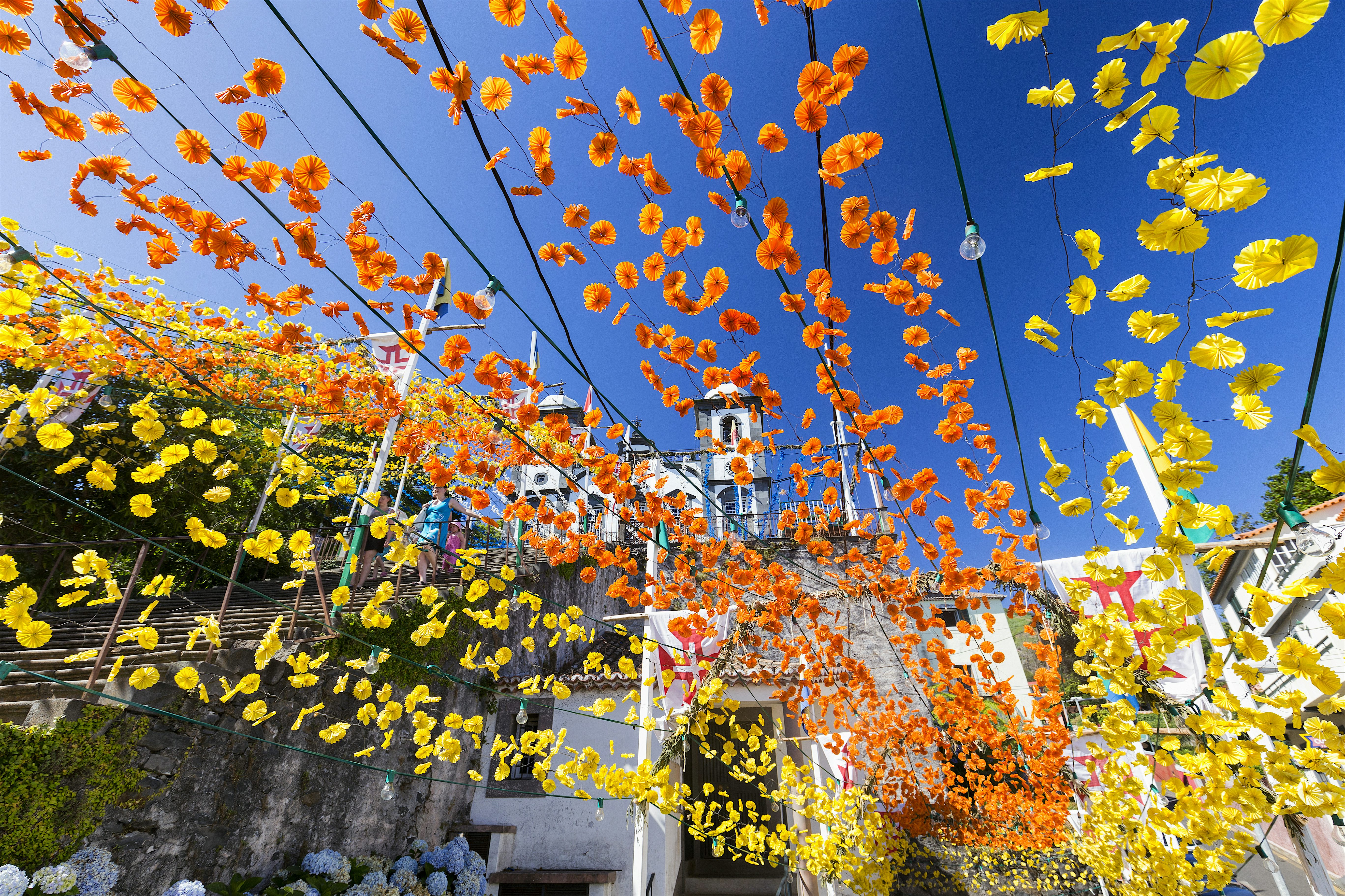 Rows of yellow and orange flower decorations at the Church of Our Lady of Monte in Funchal set to a blue sky background