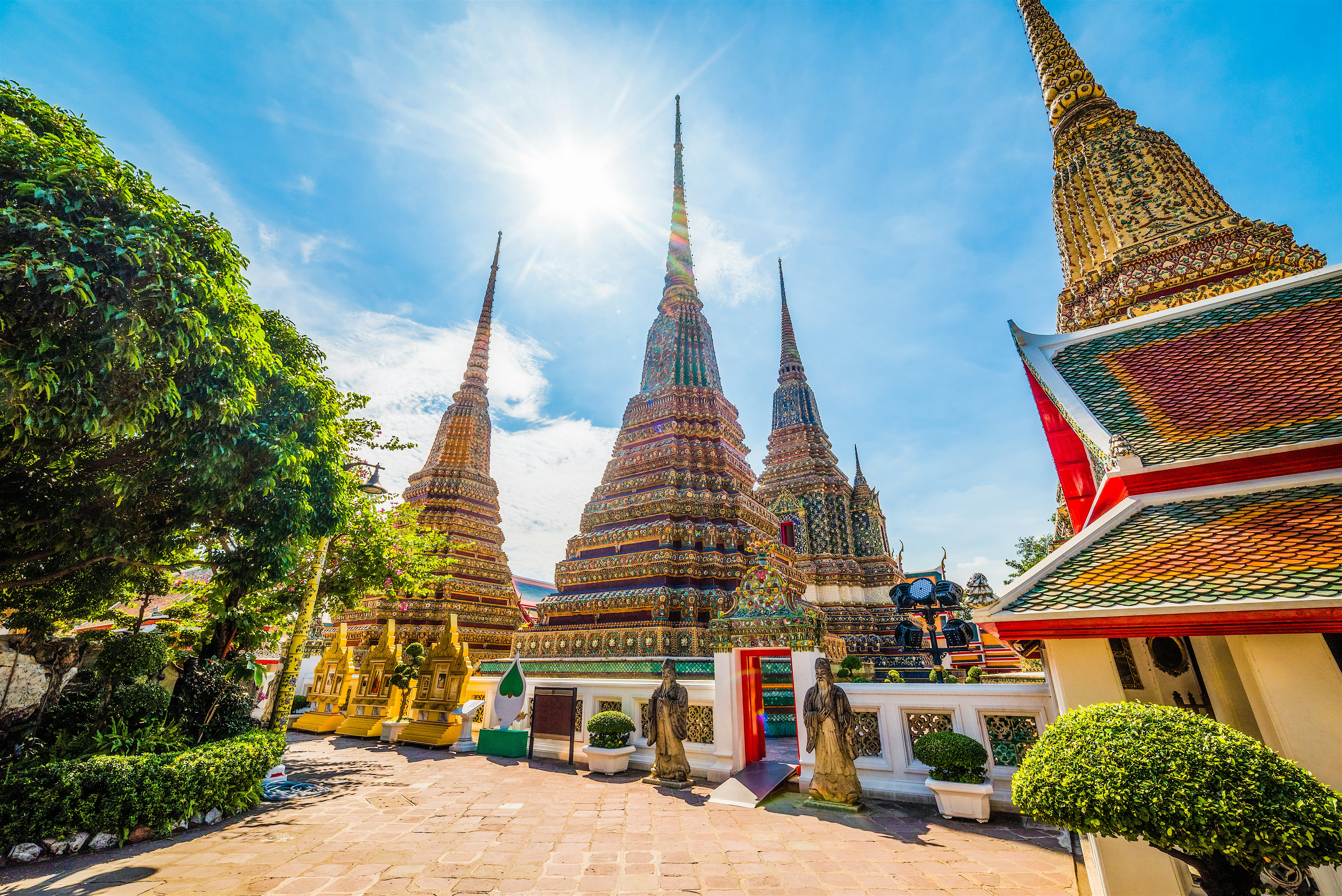 Temple of the Reclining Buddha. Four large, colourful spires (chedis) with golden statues by the front entrance