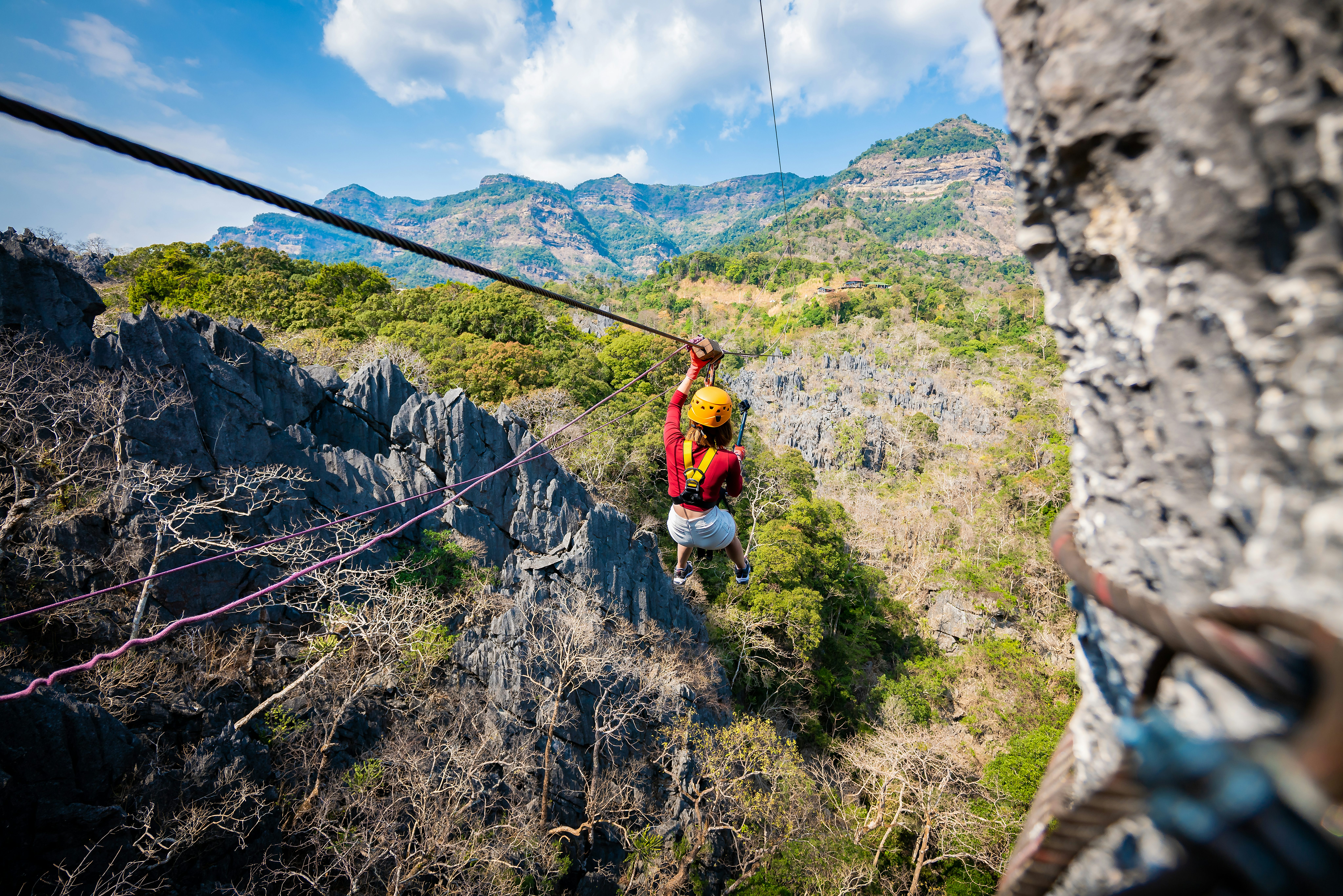 Adventure activity scene. Person zip-lining through a limestone forest mountain landscape