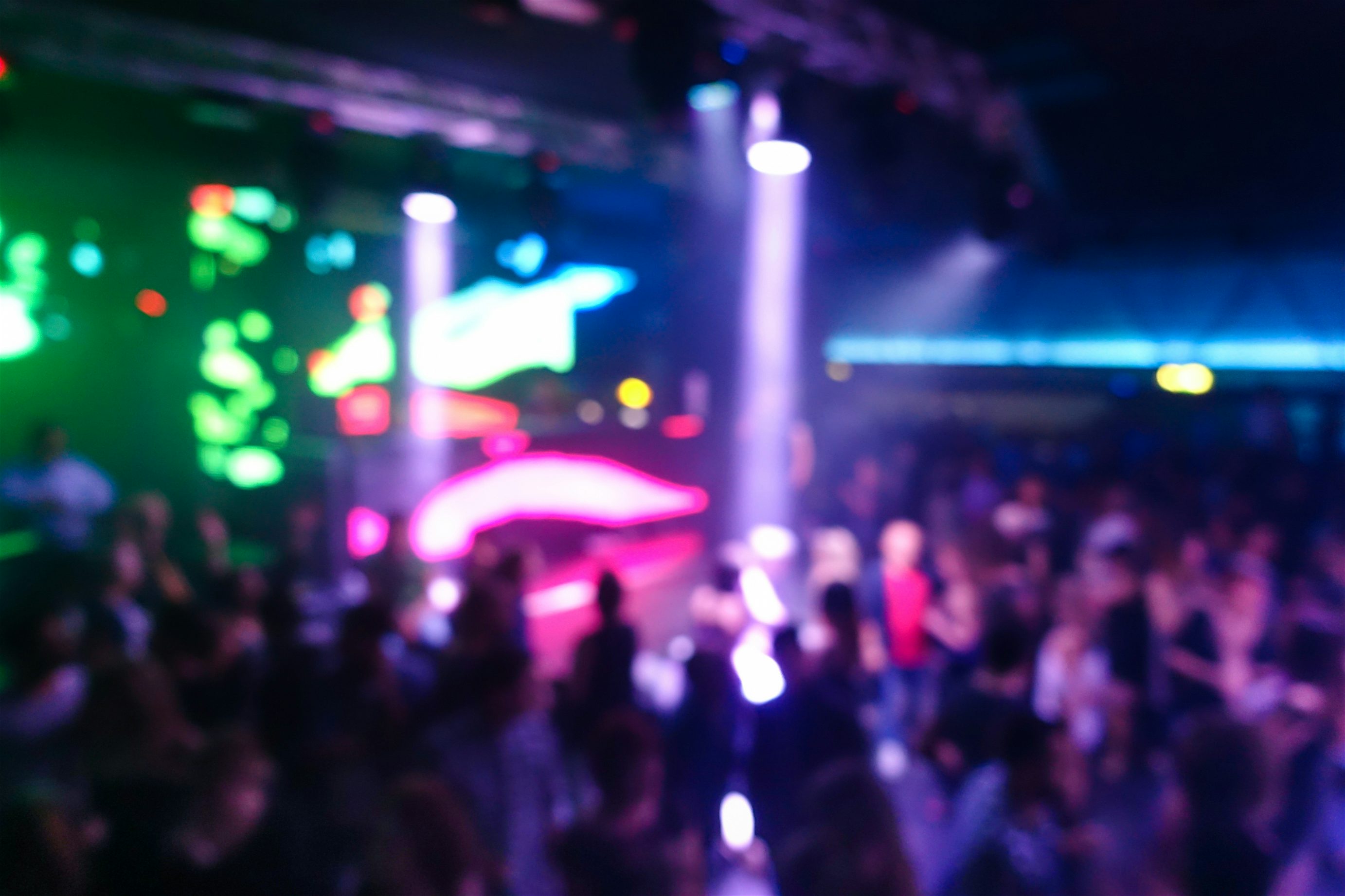 Busy night club people dancing in front of a DJ booth with purple, pink and green bright strobe lights