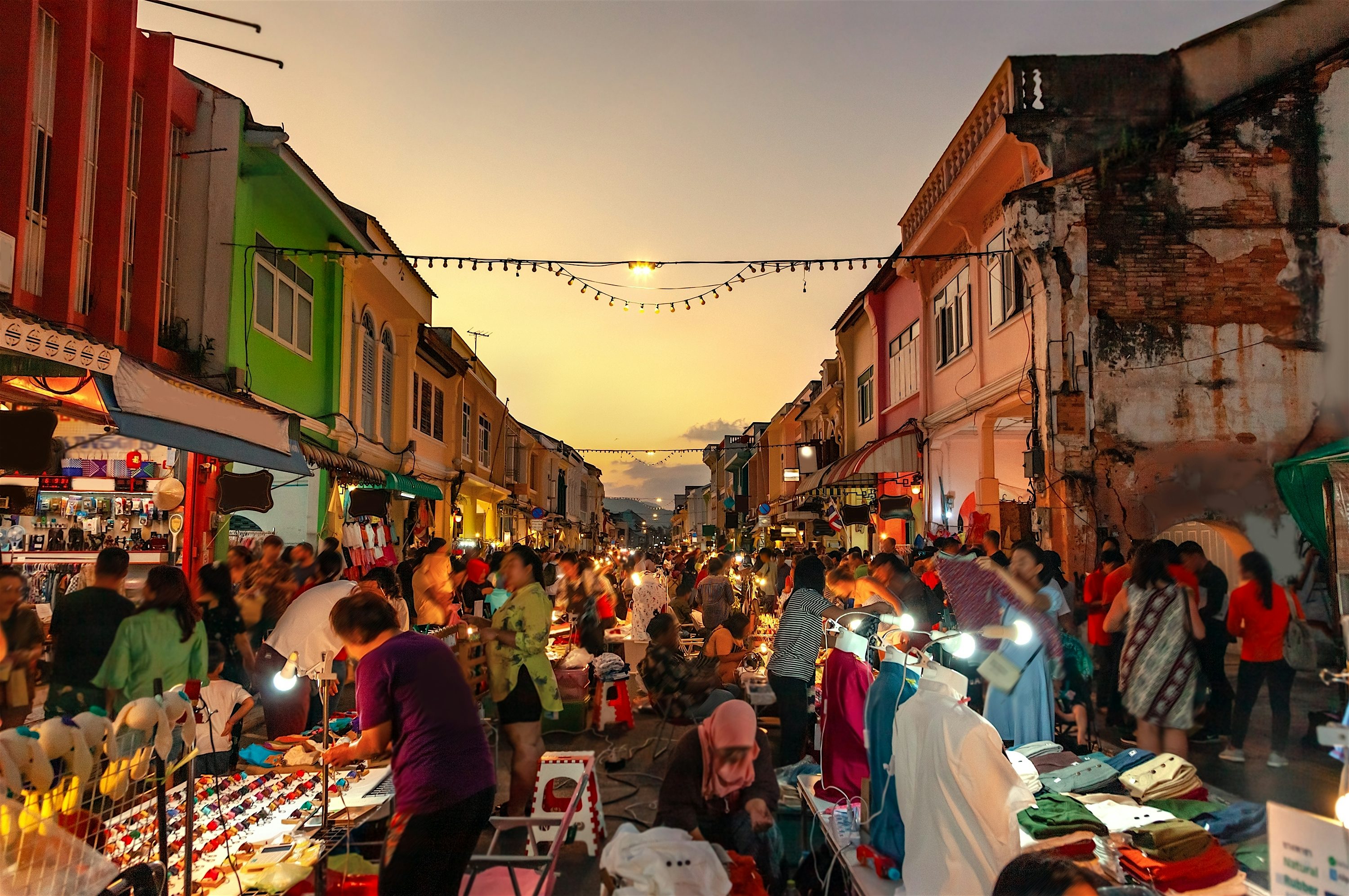 People on the street browsing market stalls at dusk with colourful buildings on either side