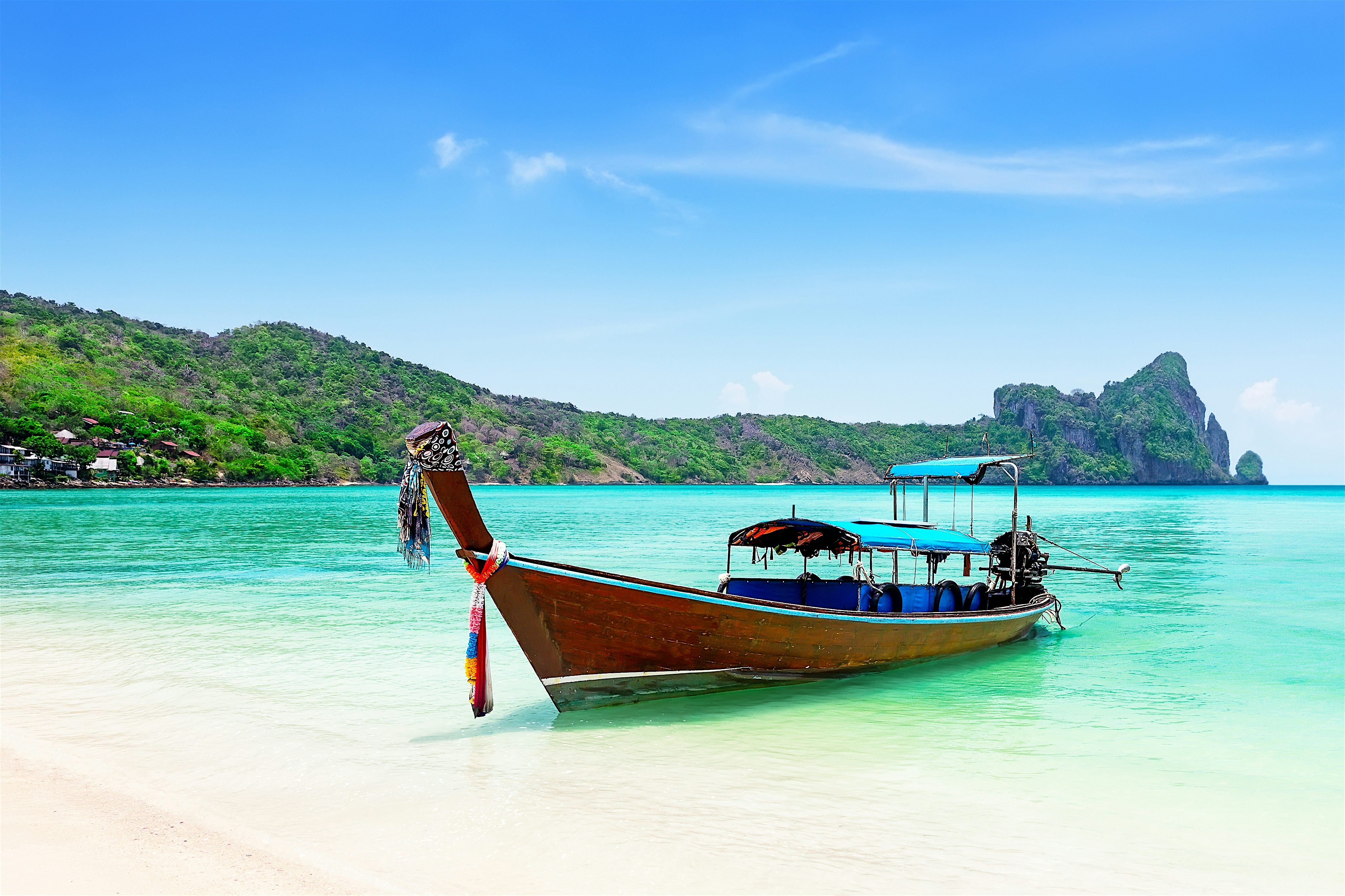 Traditional Thai longtail boat on a white sandy beach by a turquoise sea with limestone cliffs to the rear.