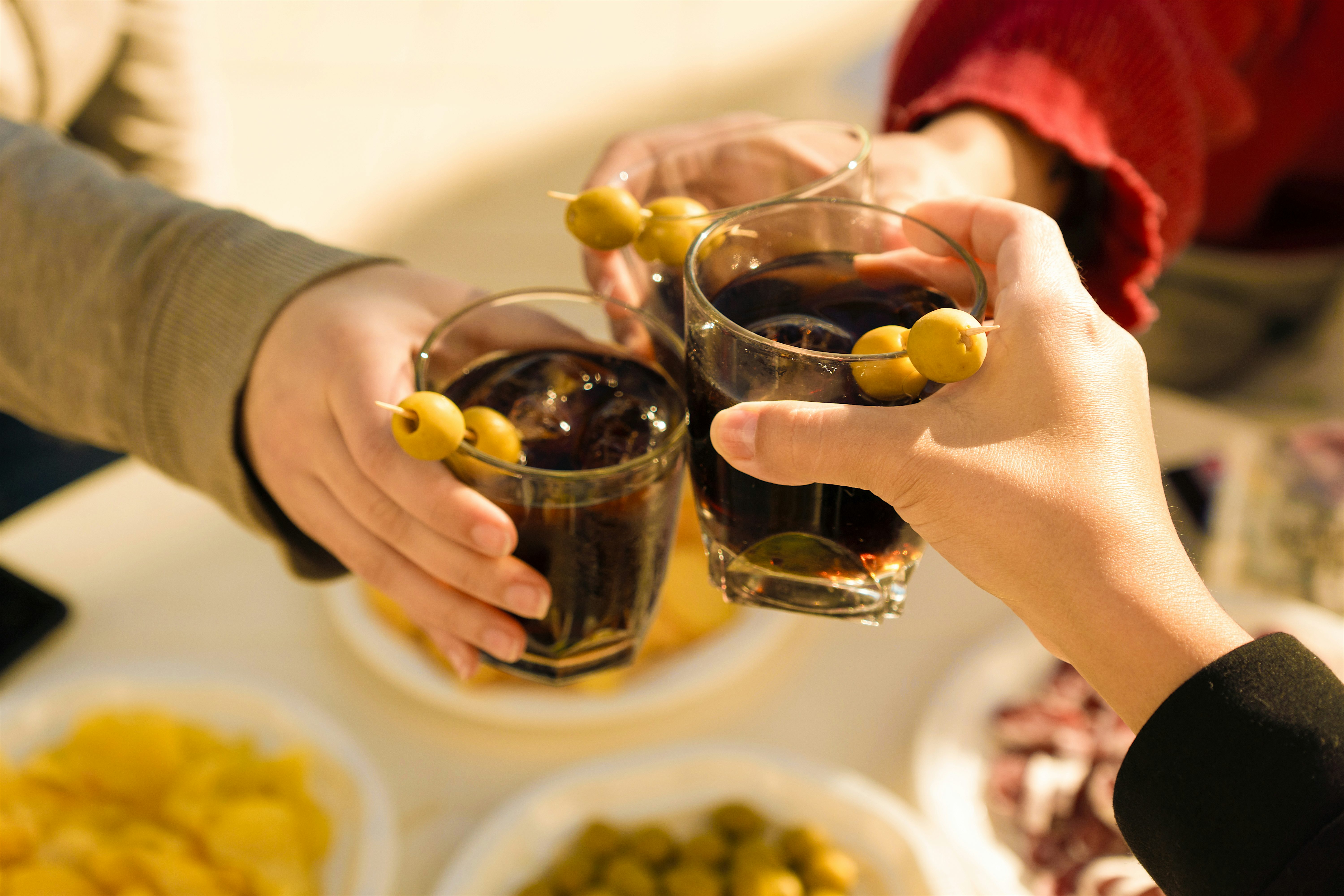 Three glasses of Vermouth clinking together, over ice with 2 olives.