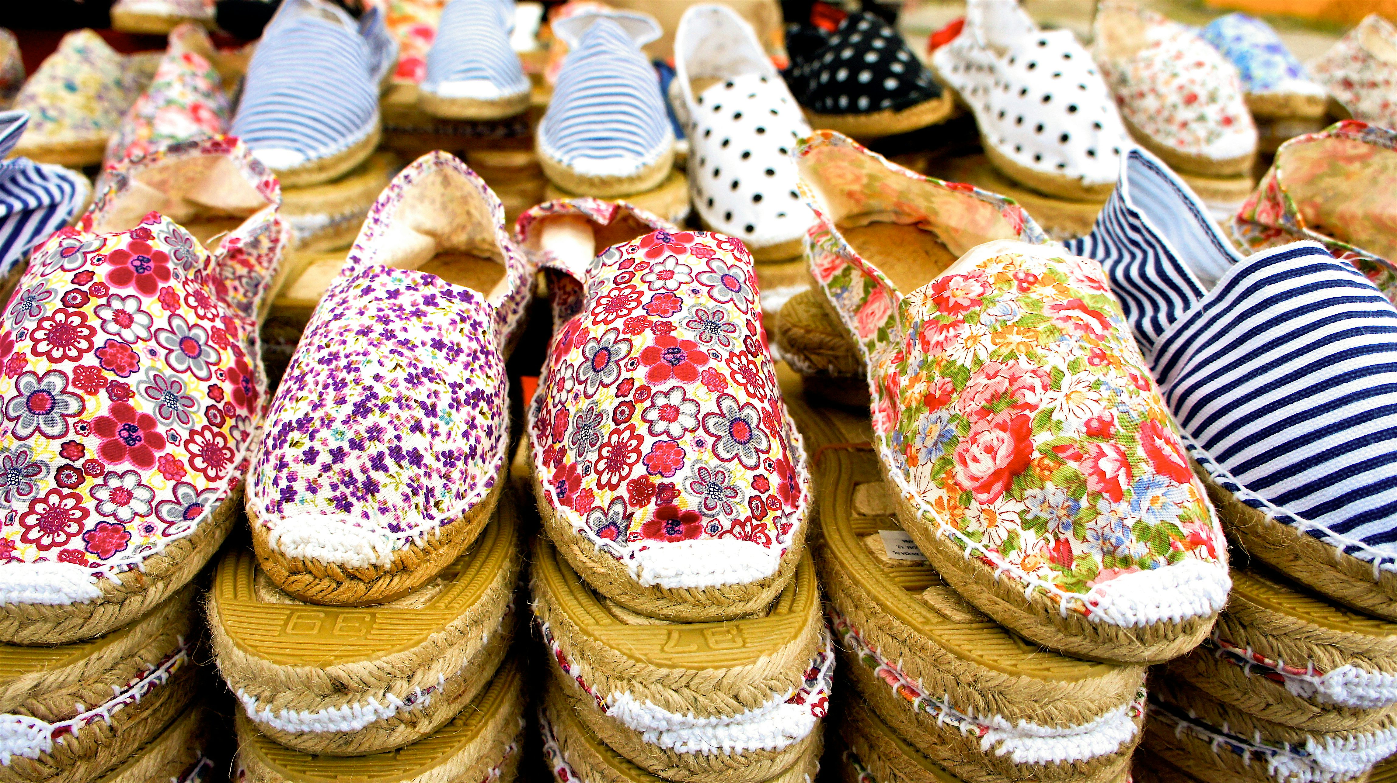 Rows of traditional, patterned espadrille shoes stacked on display, featuring floral and striped designs in bright colours