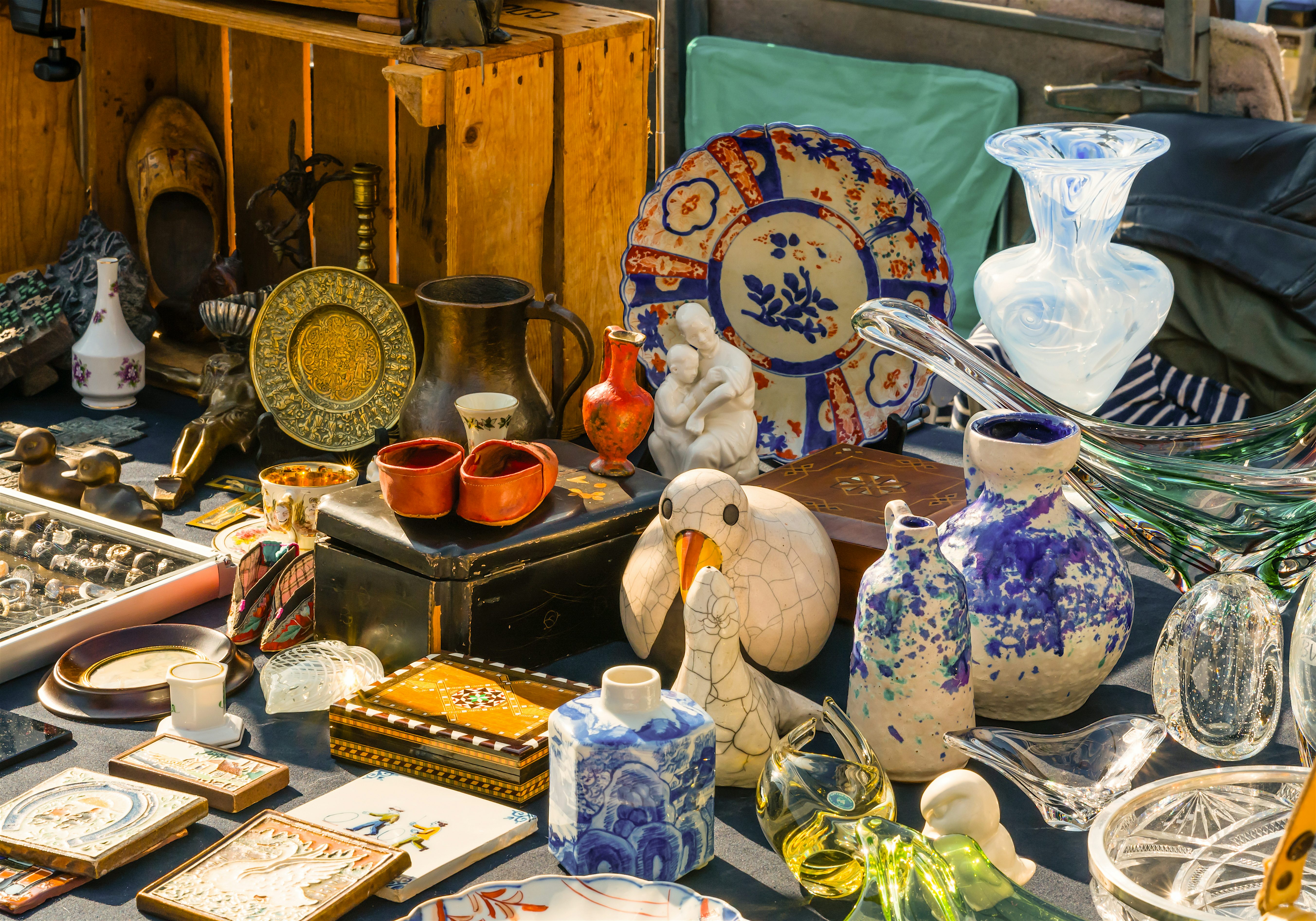 A market stall filled with vintage and decorative items, inlcuding patterned plates, glassware, vases, and small ornaments arranged closely together