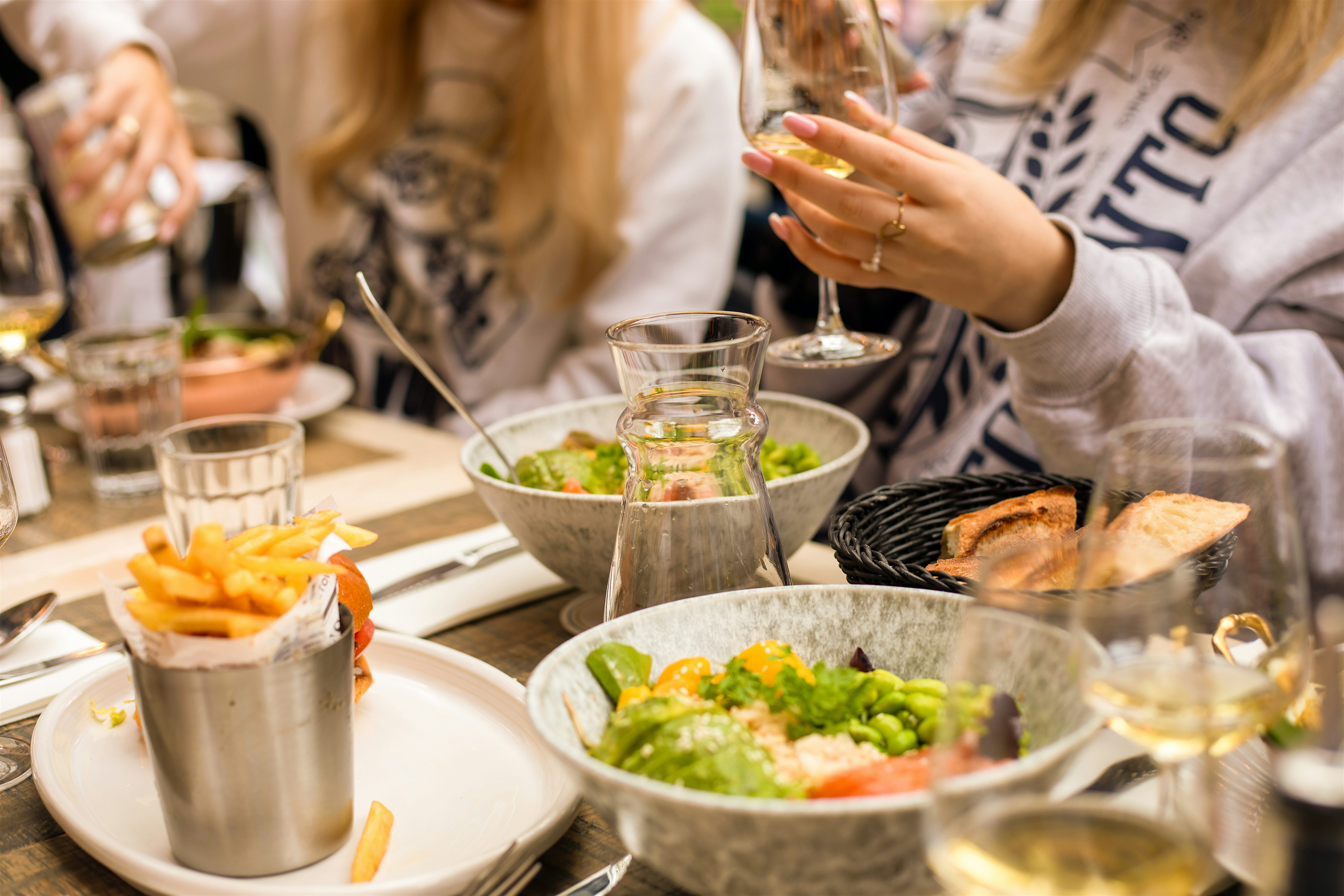 People seated at a restaurant table sharing bowls of food and drinks, with glasses of wine and plates arranged closely together.
