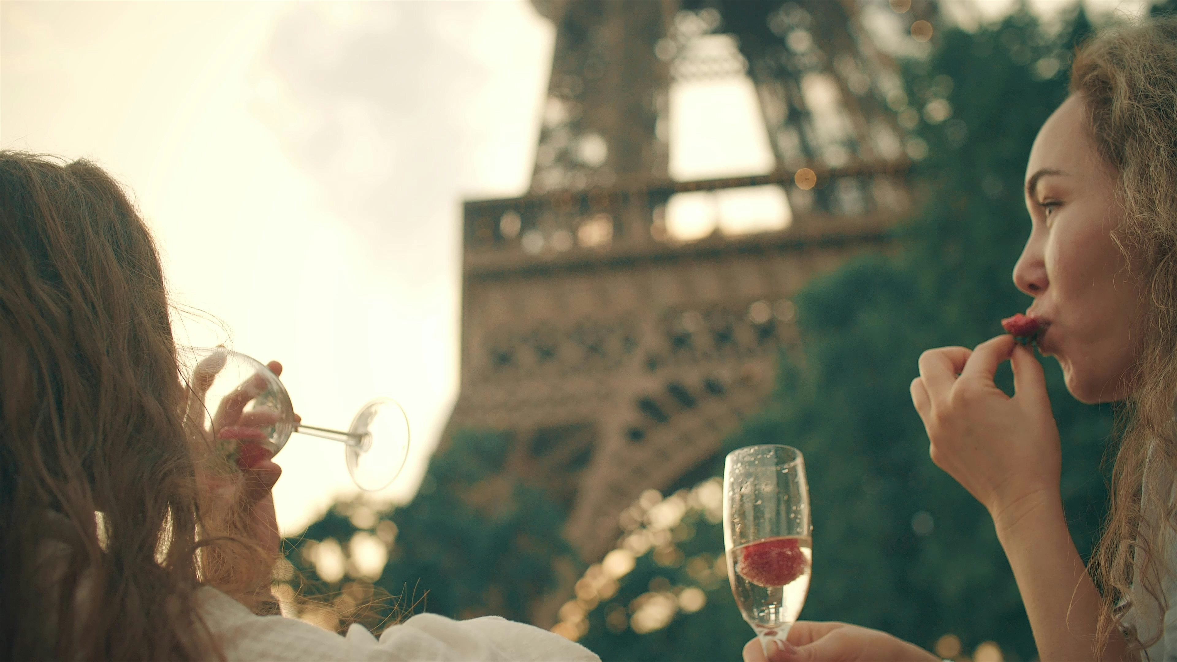 People enjoying drinks and fruit in front of the Eiffel Tower, seated outdoors with the landmark rising in the background.