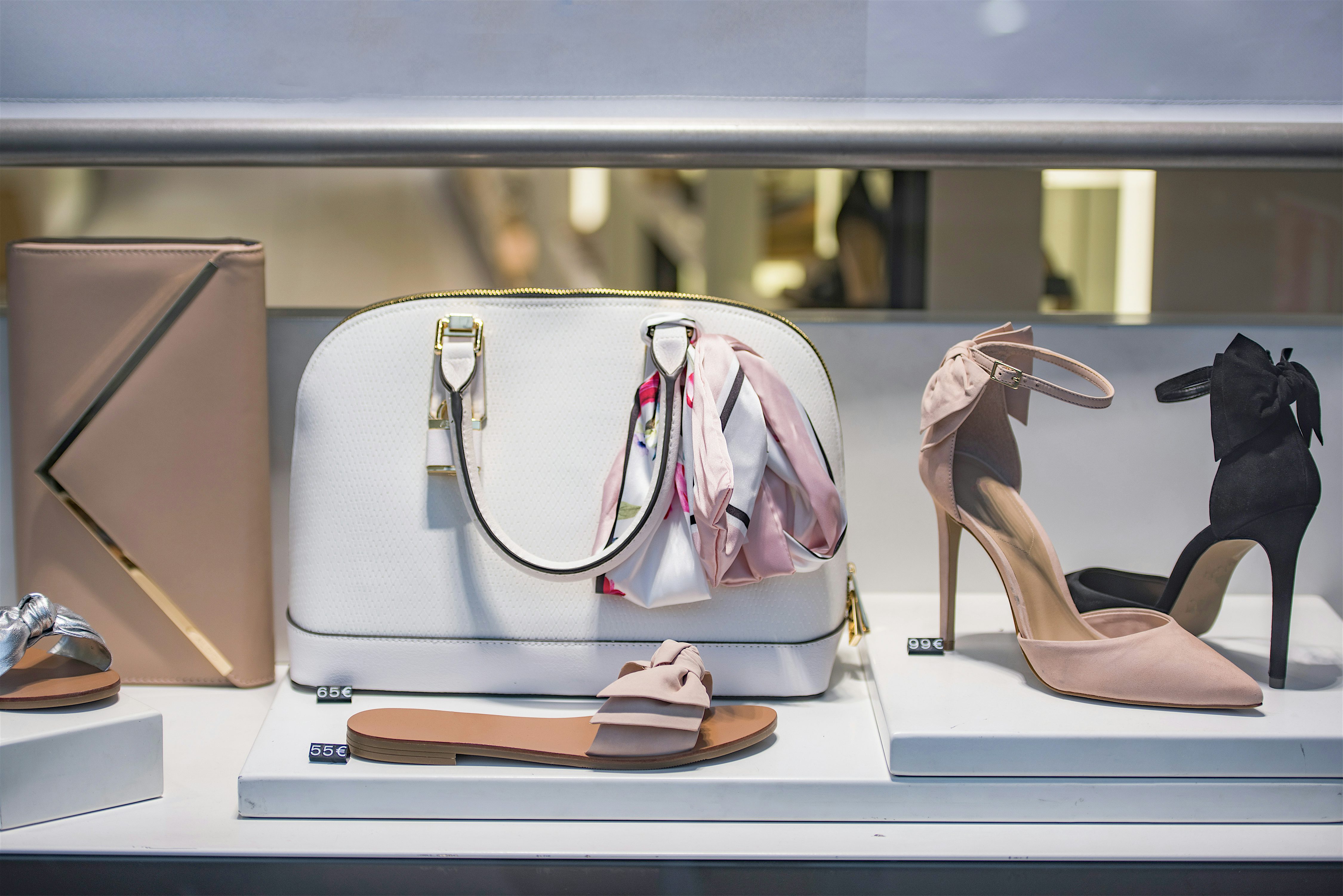 Shop window display featuring a handbag and heeled shoes in neutral tones, arranged neatly against a clean white backdrop.