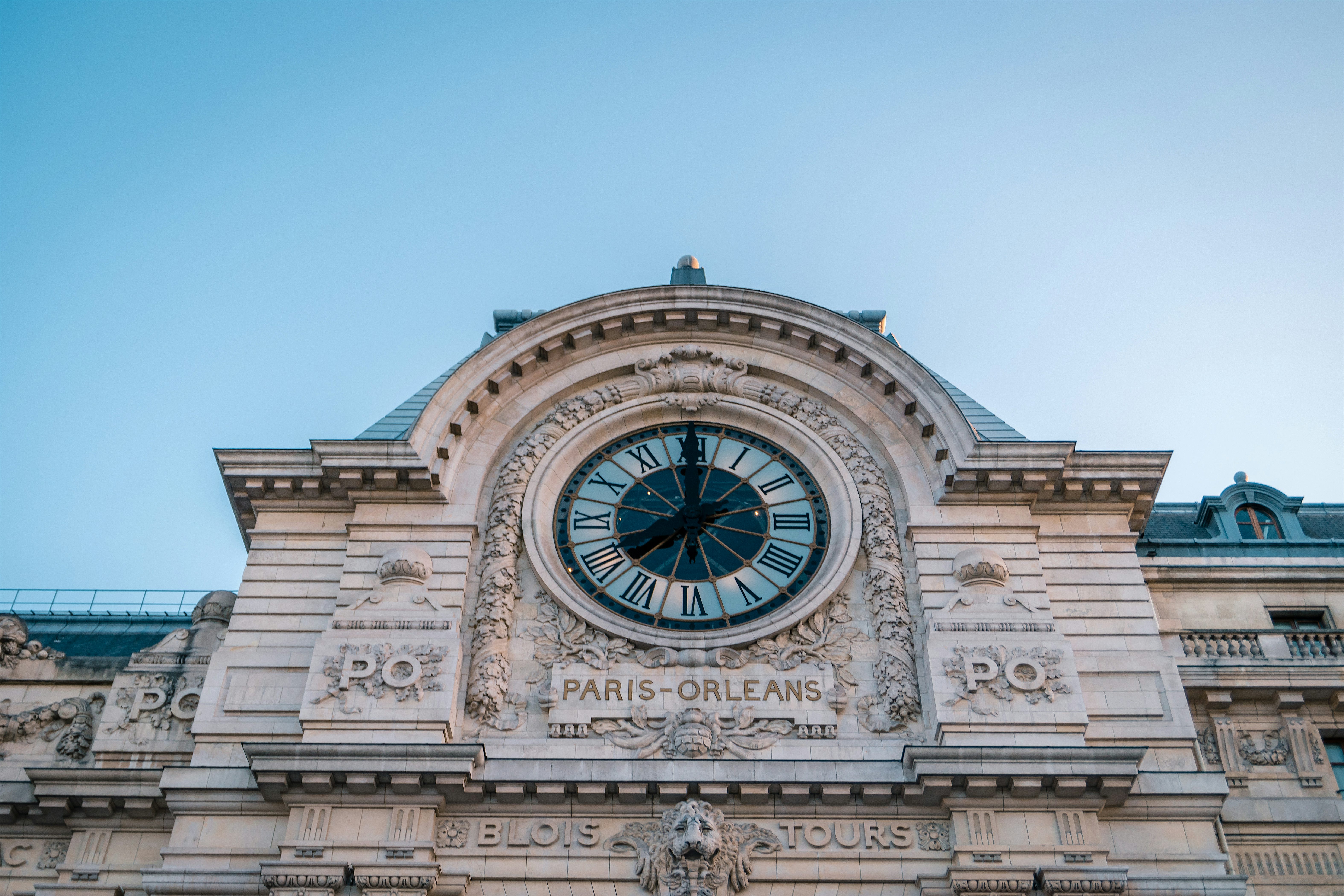Close-up of an ornate clock set into a grand stone building façade, with detailed carvings and roman numerals.