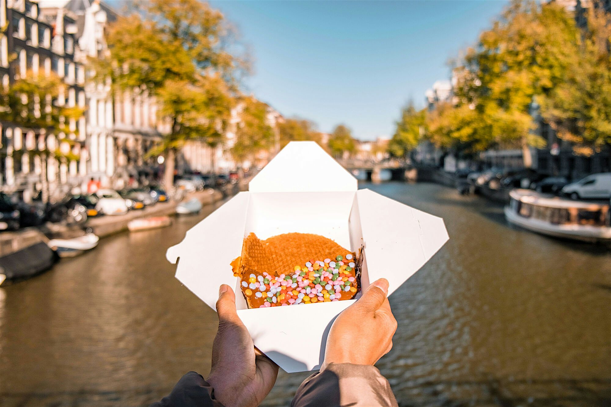 Someone holding a stroop waffle in a box with river in the background
