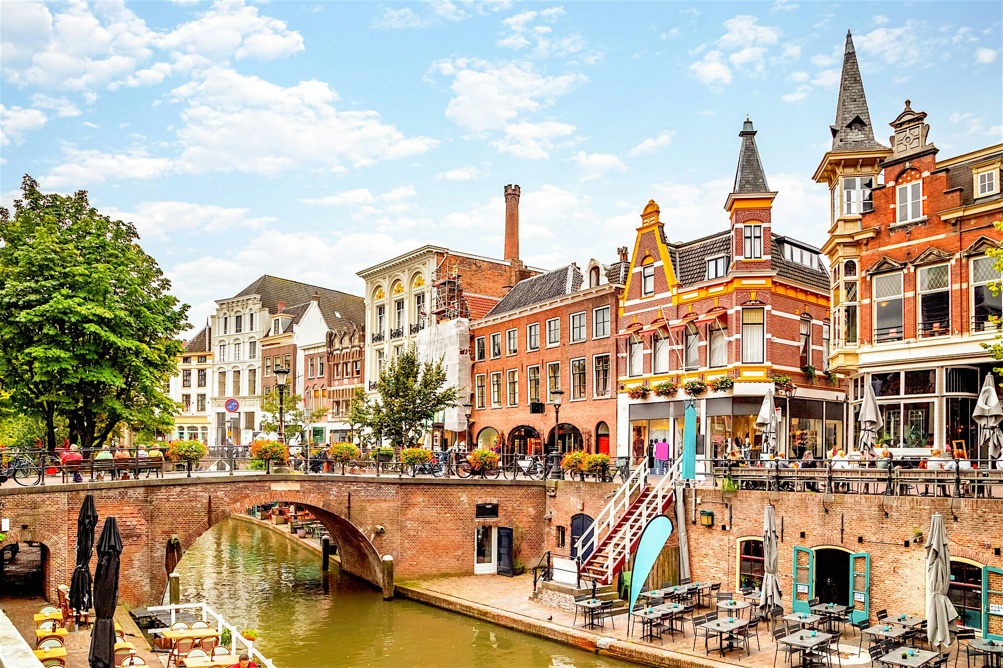 Historic canal lined with colourful, ornate buildings and cafés, with an arched brick bridge crossing the water