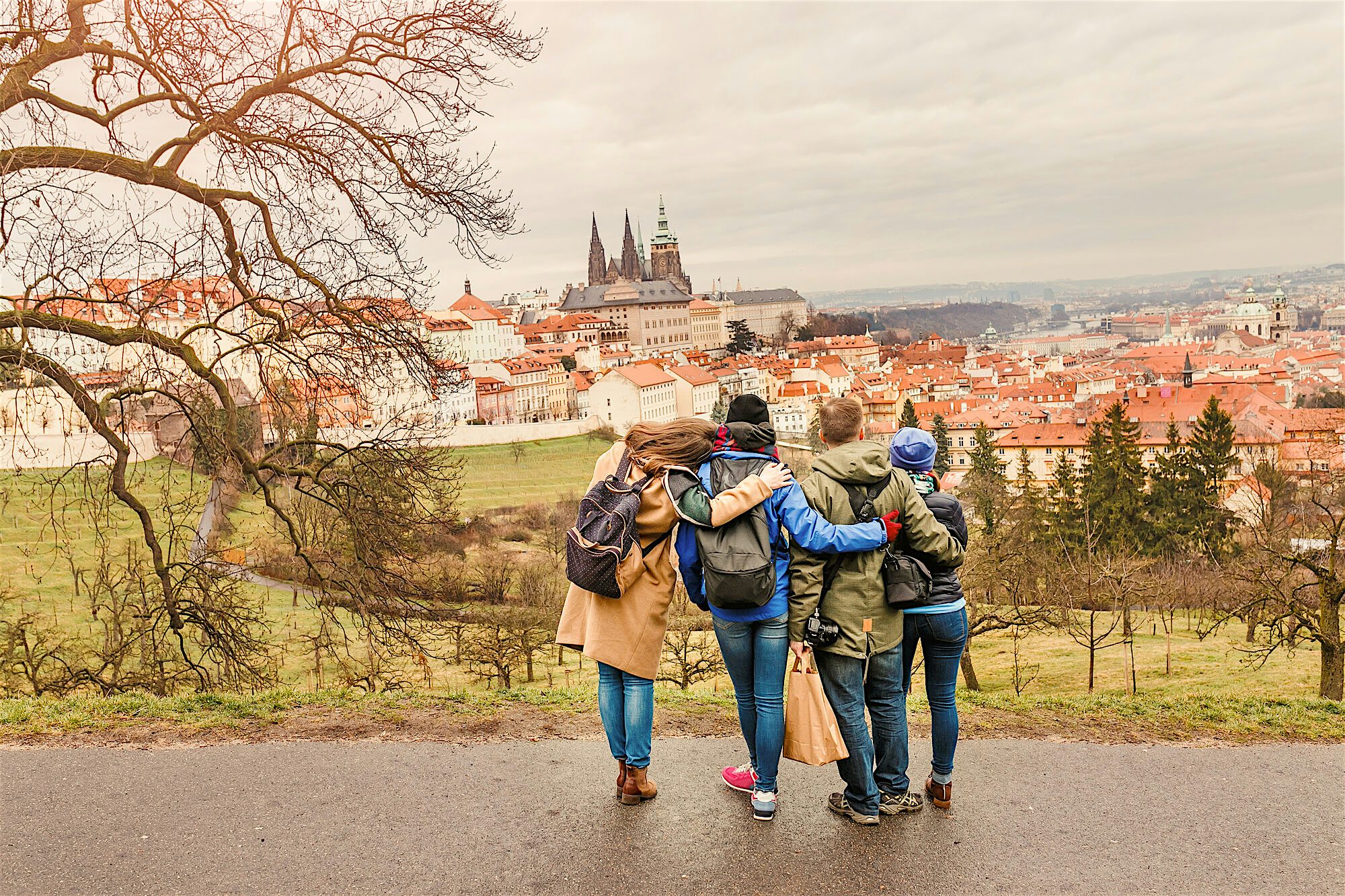 Small group walking arm in arm along a hillside path, overlooking a city of red rooftops and church spires spread out below.
