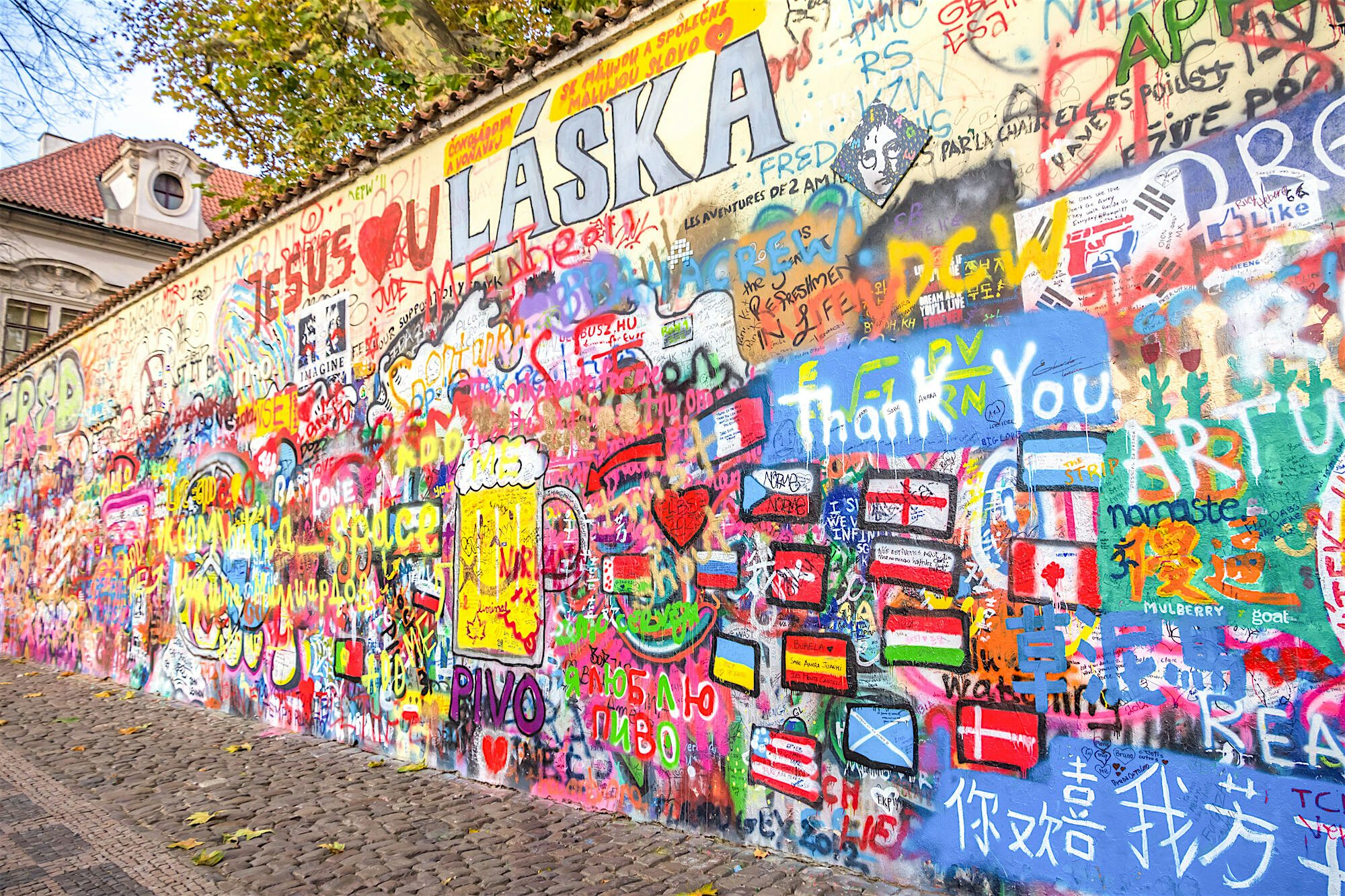 Long wall covered in layered graffiti, hand-painted messages, flags, and symbols in bright overlapping colours.