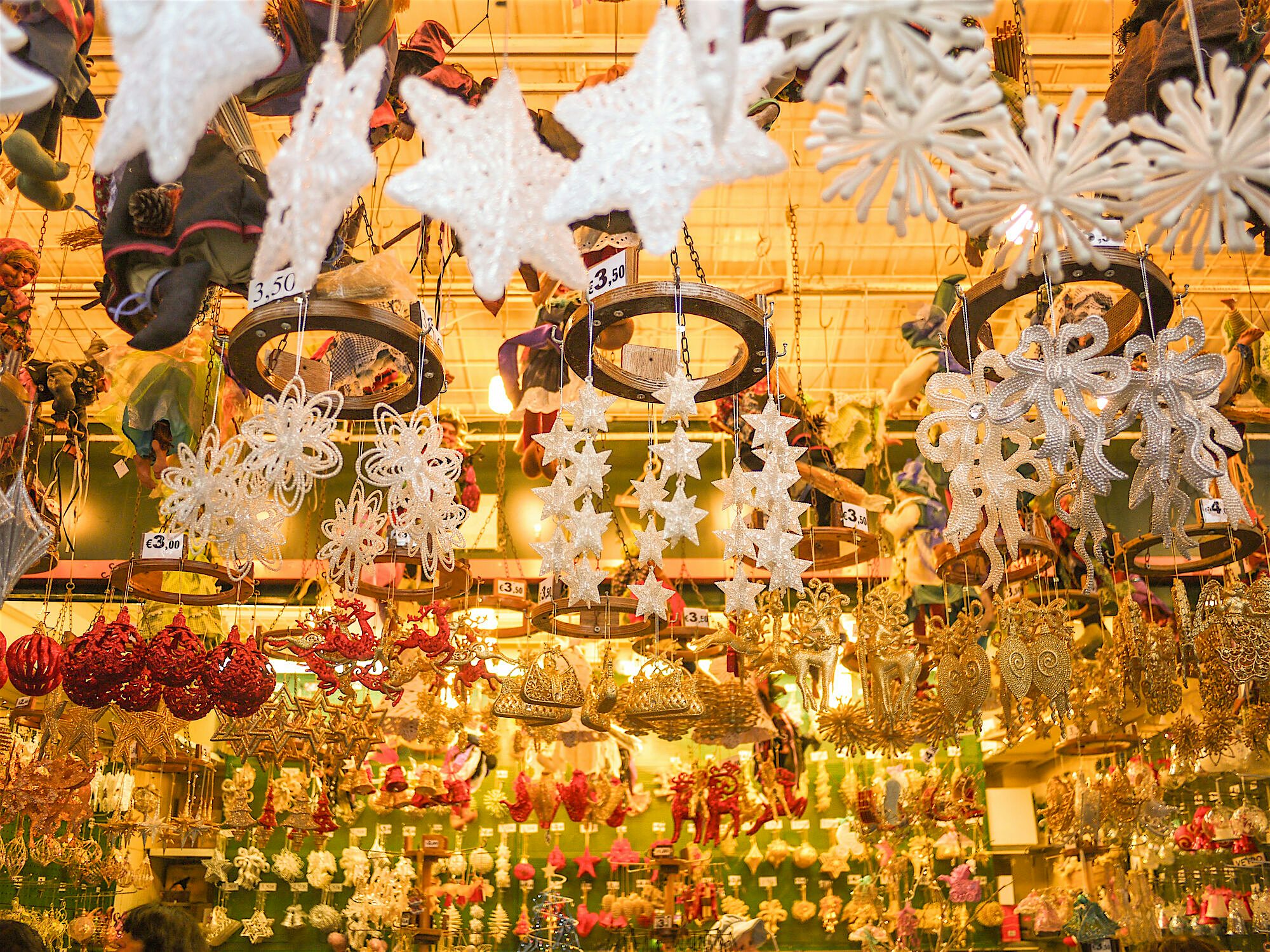 "A festive market stall filled with hanging decorative ornaments, including snowflakes and baubles, displayed under warm lighting.  "