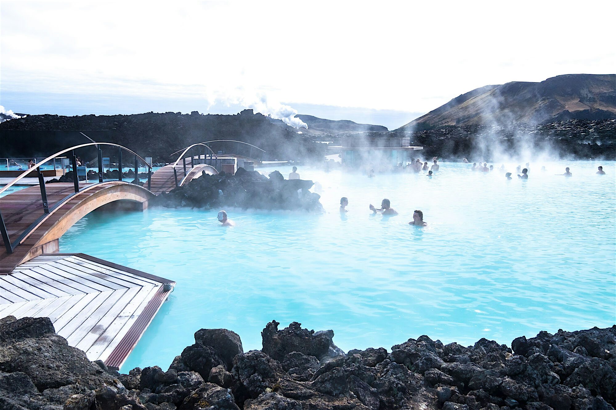 People in the Blue Lagoon geothermal spa surrounded by black volcanic rocks