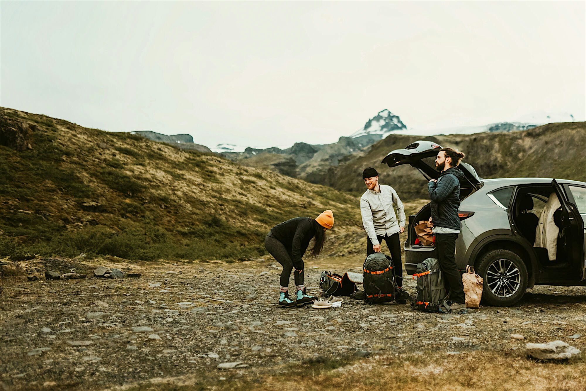 Group preparing for a hike with backpacks by a car to a background of rugged terrain