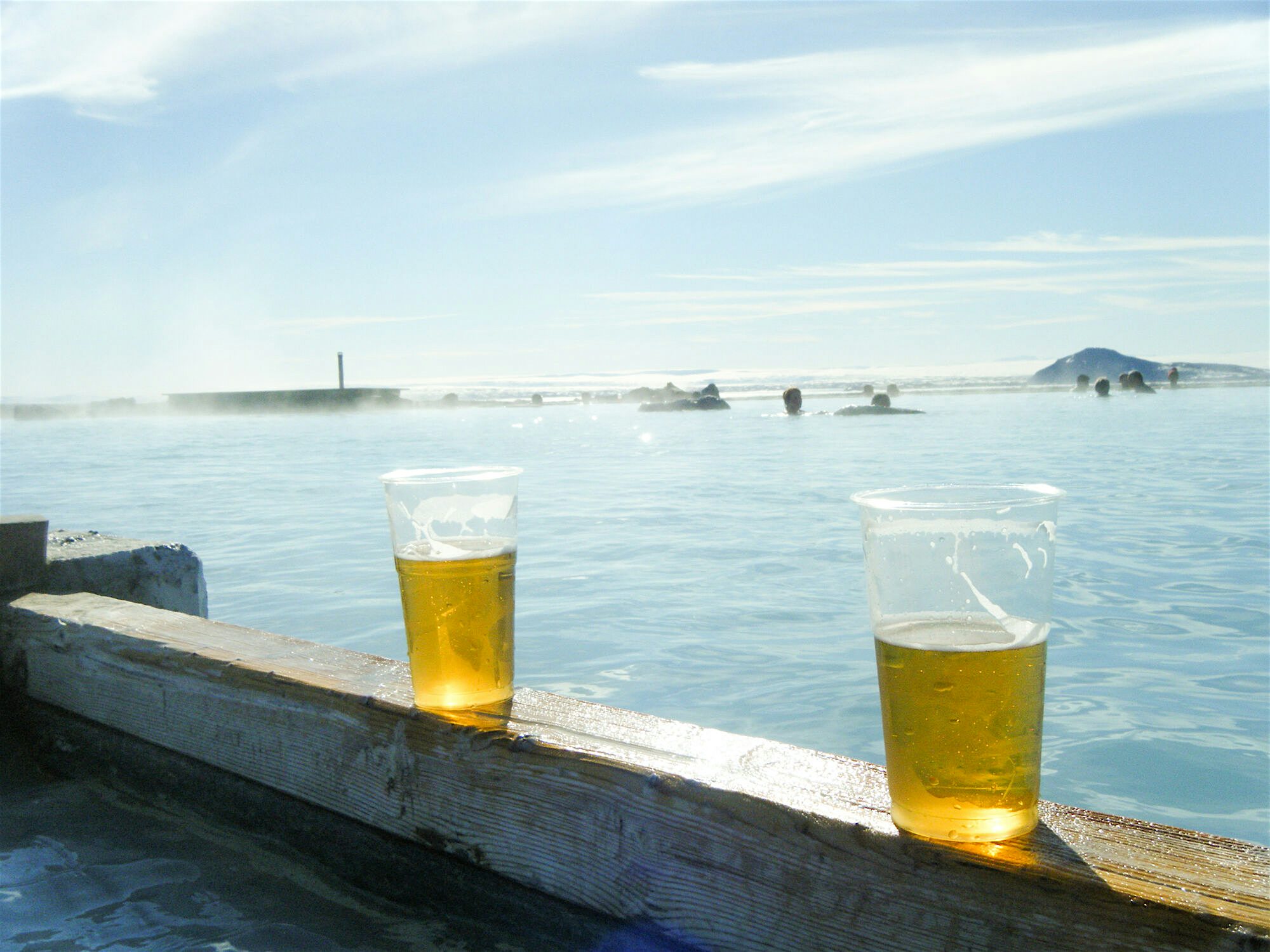 Two half drunk pints of beer on a wooden plank at the edge of a geothermal spa