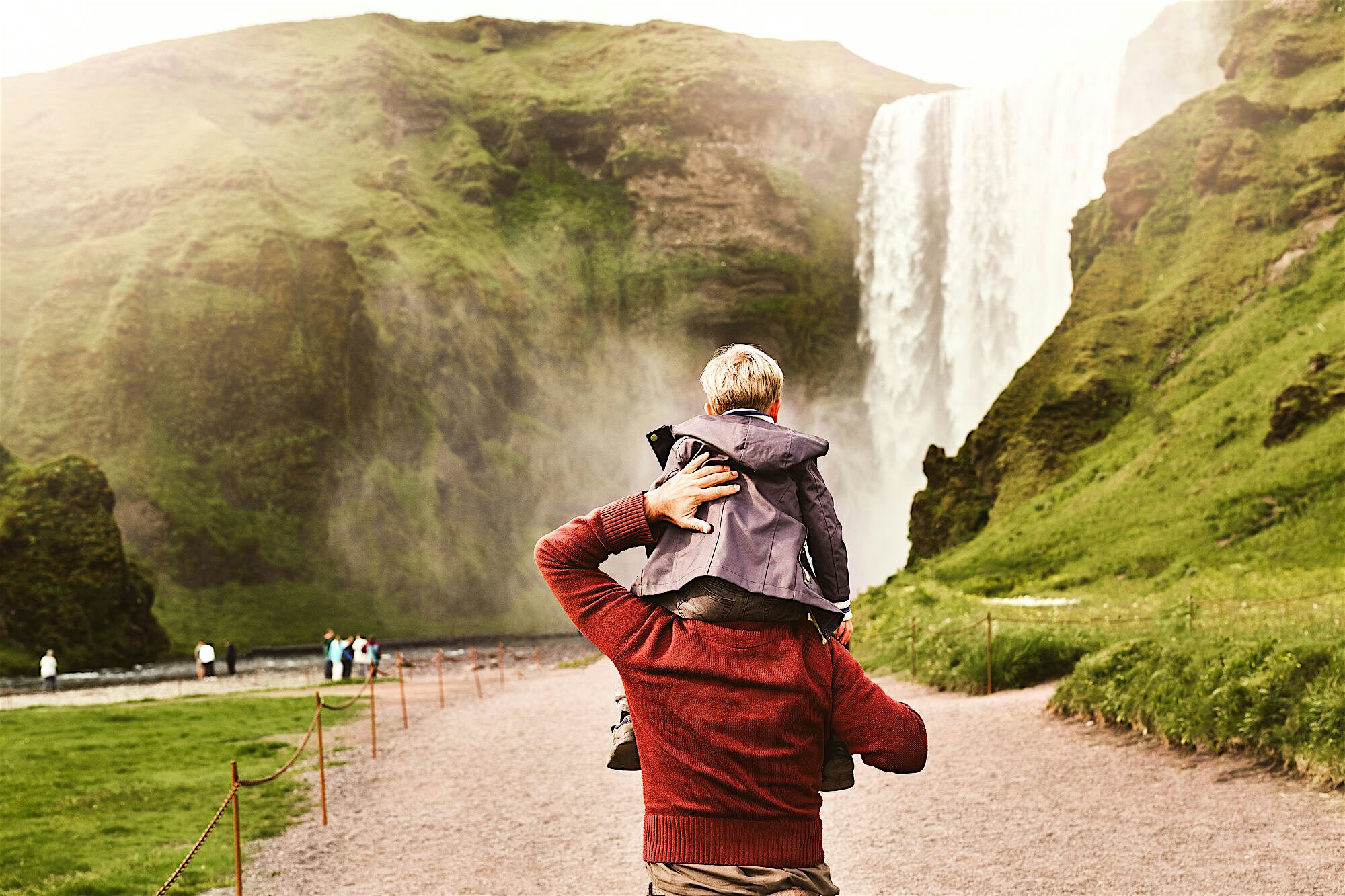Child on the shoulders of his father walking towards the iconic waterfall Skógafoss